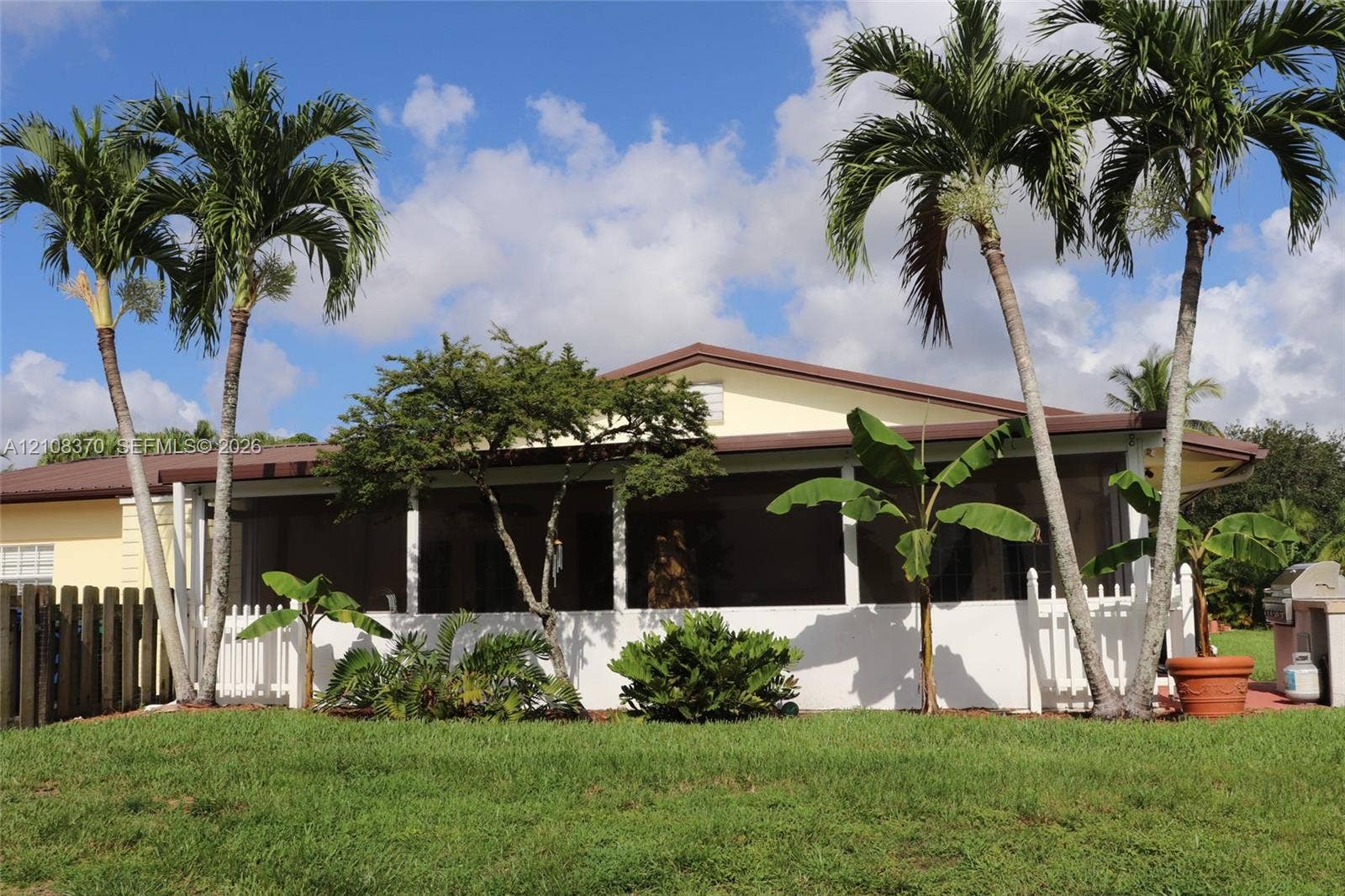 18901 SW 63rd Street, Southwest Ranches, FL 33332 Exterior space featuring a large screened-in porch, white picket fencing, mature palm trees, and a built-in outdoor cooking station
