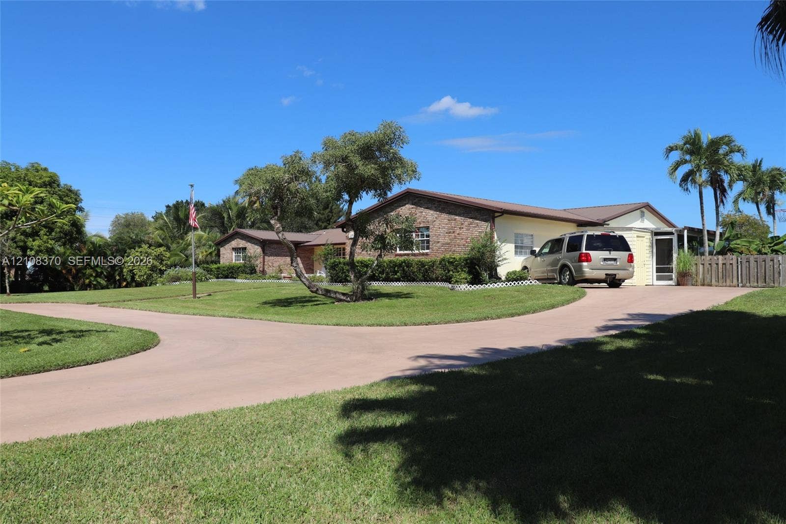 18901 SW 63rd Street, Southwest Ranches, FL 33332 Single-story residence featuring a brick facade, multi-gabled roofline, sprawling manicured lawn, curved concrete driveway, and mature landscaping
