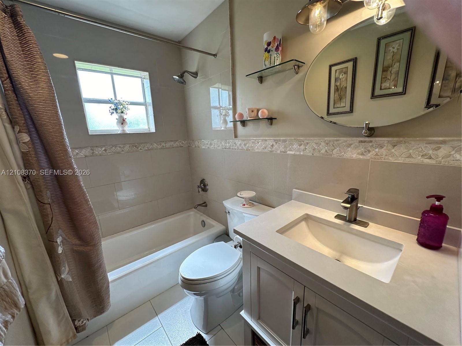 18901 SW 63rd Street, Southwest Ranches, FL 33332 Bathroom featuring a vanity with a solid-surface countertop, an integrated sink, an oval wall-mounted mirror, neutral tile wall surround with decorative accent inlay, and a tub-shower combination