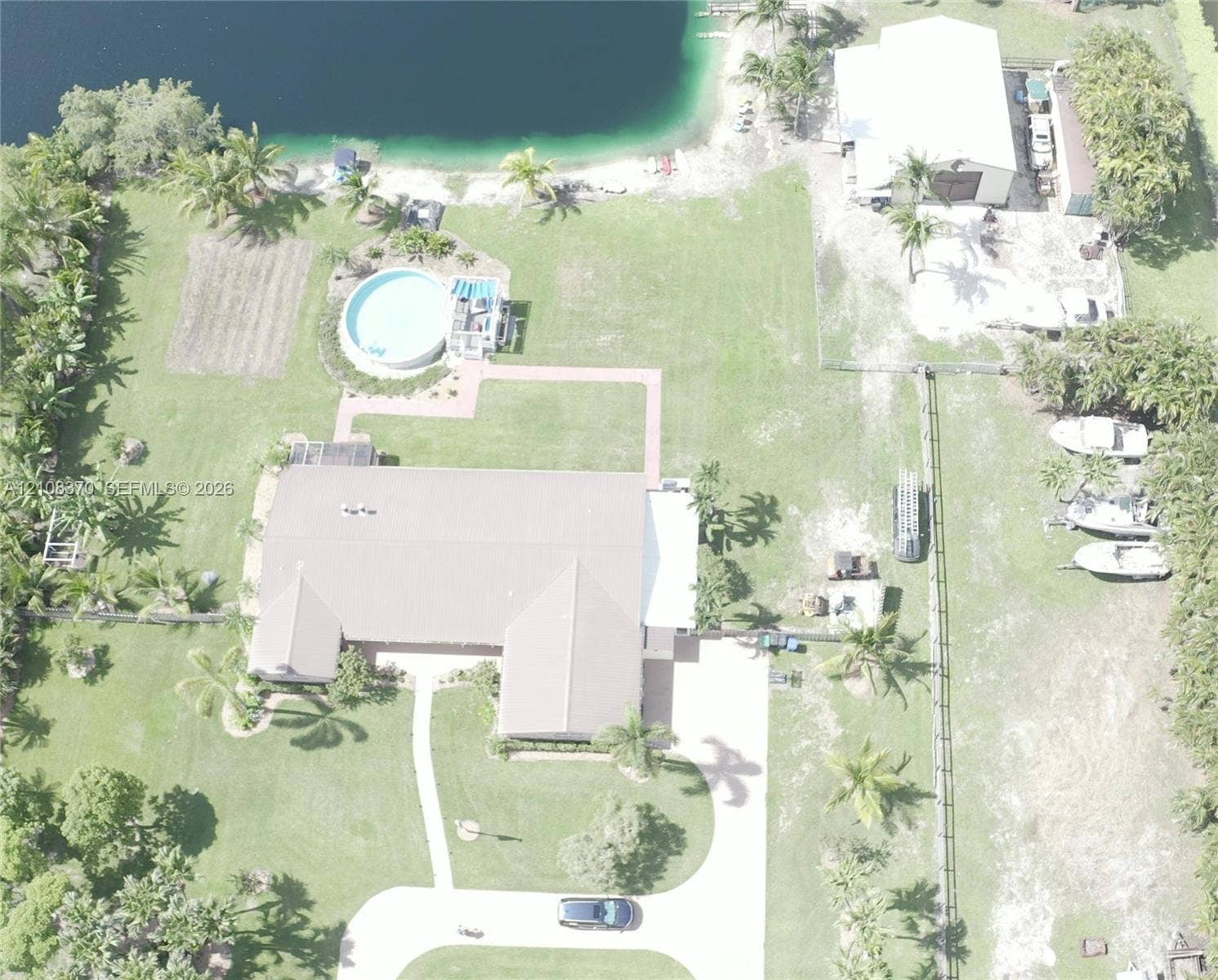 18901 SW 63rd Street, Southwest Ranches, FL 33332 Waterfront property featuring a detached garage, a circular above-ground pool, a concrete driveway, and expansive lawn space