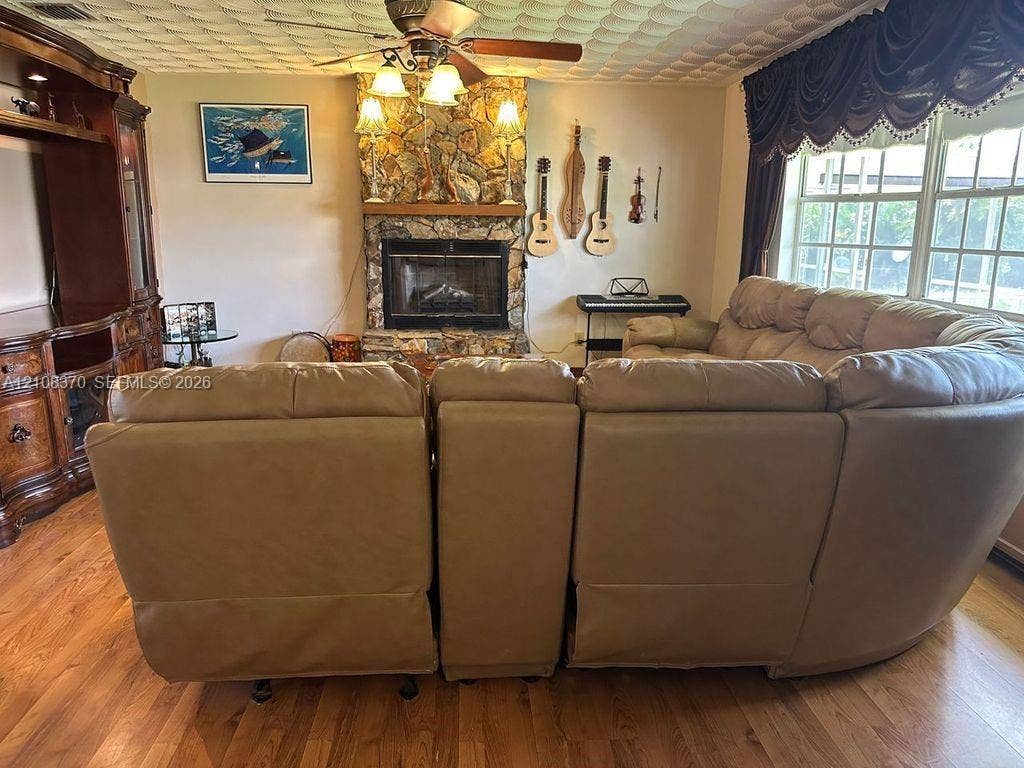 18901 SW 63rd Street, Southwest Ranches, FL 33332 Floor-to-ceiling stone fireplace featuring a wood mantel, integrated wood-finish cabinetry, wood-finish flooring, and a ceiling-mounted light fixture with a fan