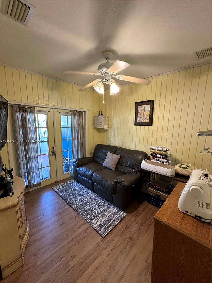 18901 SW 63rd Street, Southwest Ranches, FL 33332 Vertical wood-paneled walls, wood-finish flooring, double-lite glass doors, and a ceiling fan with integrated light fixture