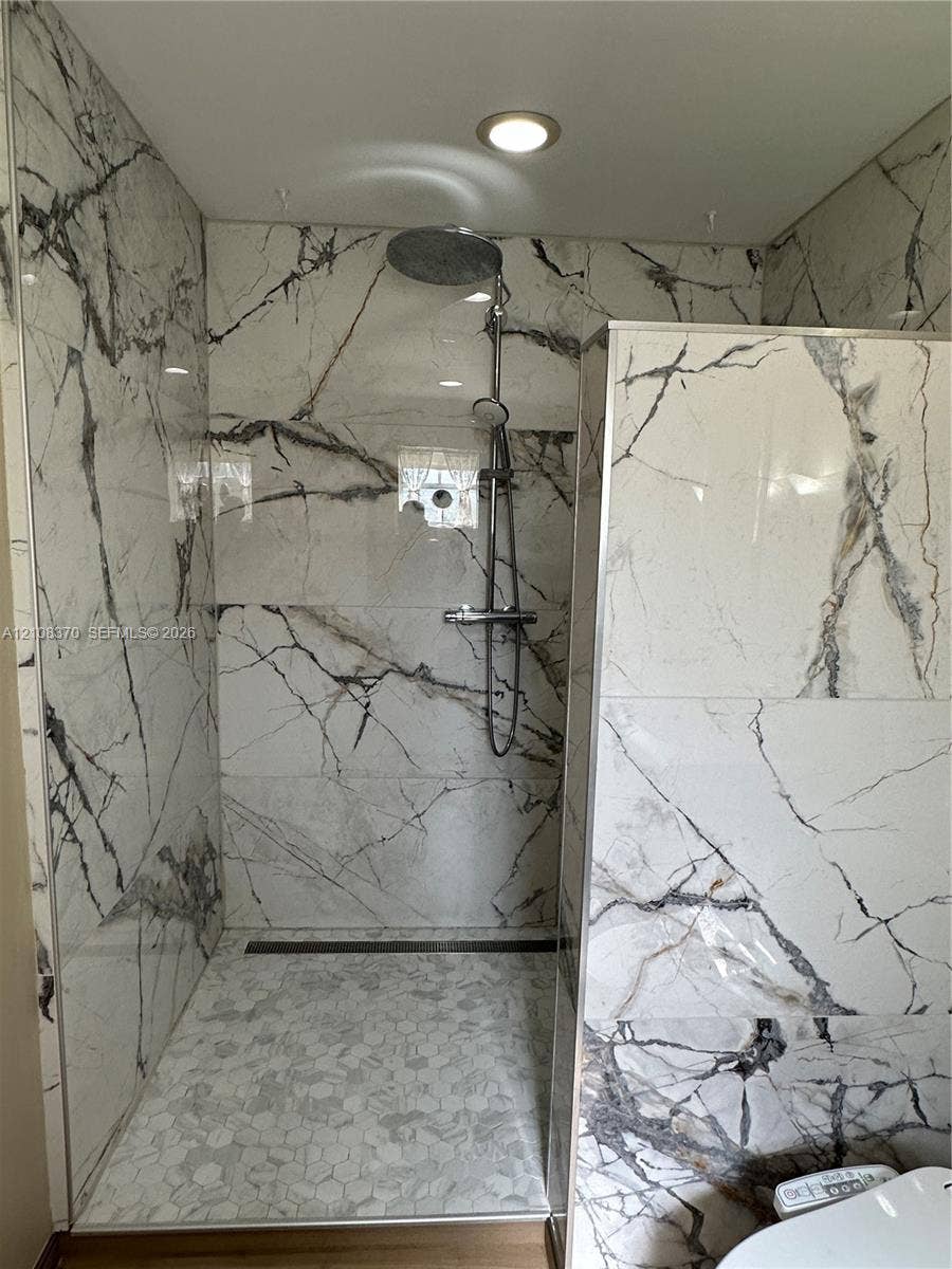 18901 SW 63rd Street, Southwest Ranches, FL 33332 Walk-in shower featuring large-format stone-finish wall tile, hexagonal floor tiling, a rainfall showerhead, and a linear floor drain