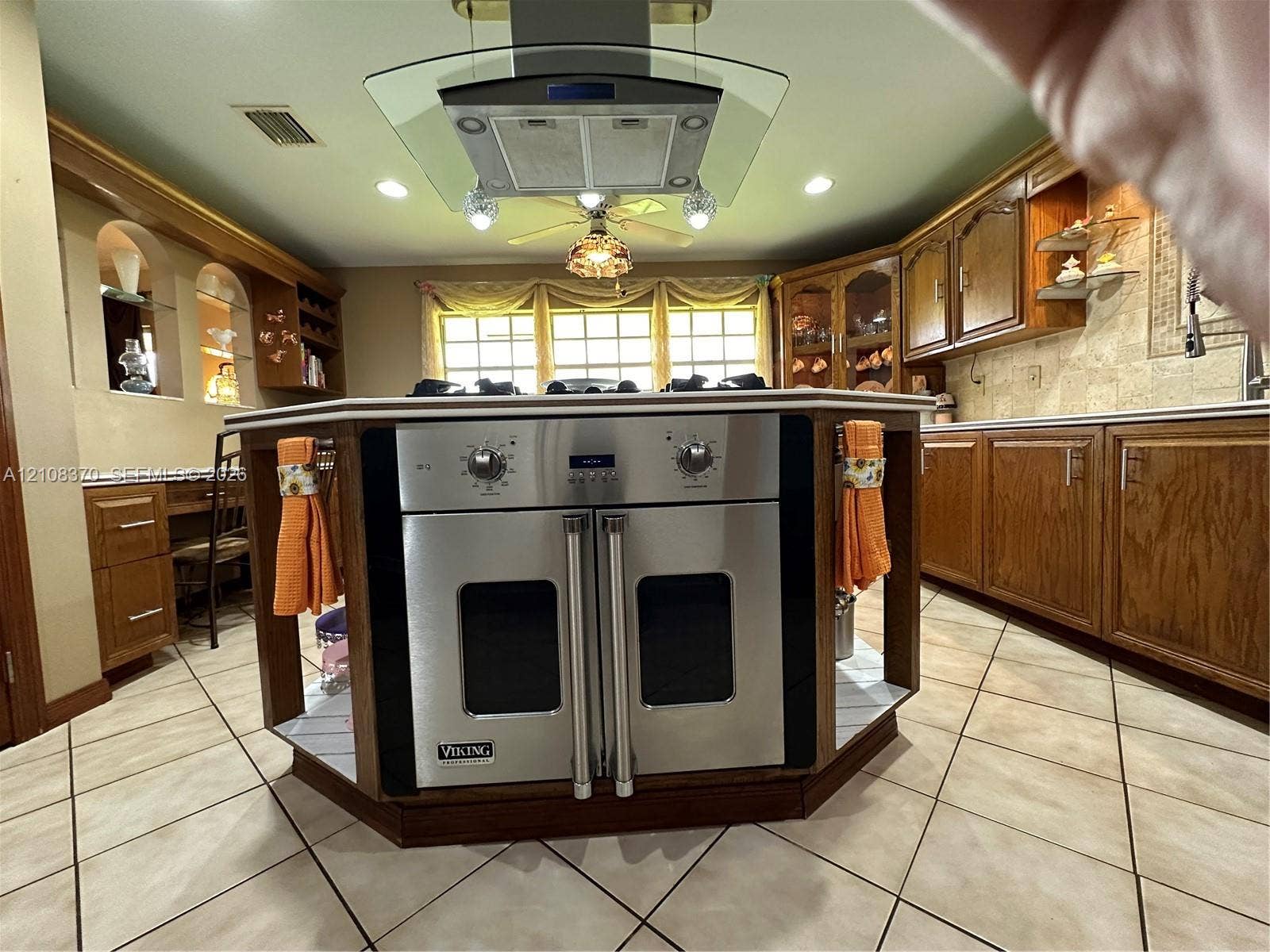 18901 SW 63rd Street, Southwest Ranches, FL 33332 Kitchen featuring a central island with a built-in stainless steel double oven, glass-paned range hood, tile flooring, and custom cabinetry with integrated shelving