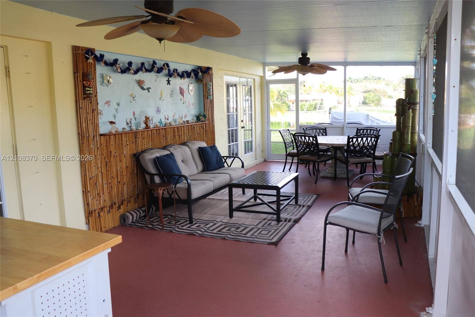 18901 SW 63rd Street, Southwest Ranches, FL 33332 Screened-in porch featuring painted concrete flooring, bamboo-paneled wall accent, dual ceiling fans, and double-door entry
