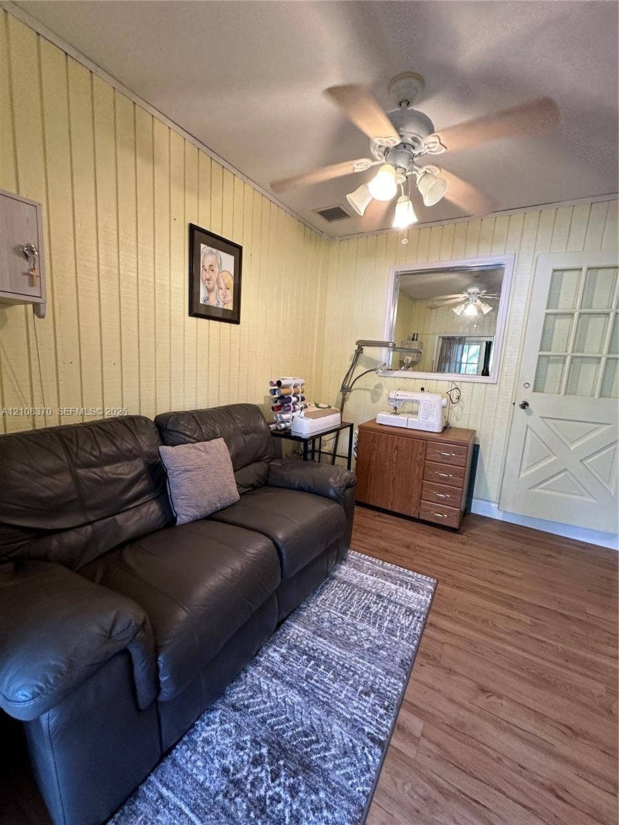 18901 SW 63rd Street, Southwest Ranches, FL 33332 Vertical wood-plank wall paneling, light-toned wood-finish flooring, ceiling fan with integrated multi-light fixture, and a multi-pane door with X-pattern detailing