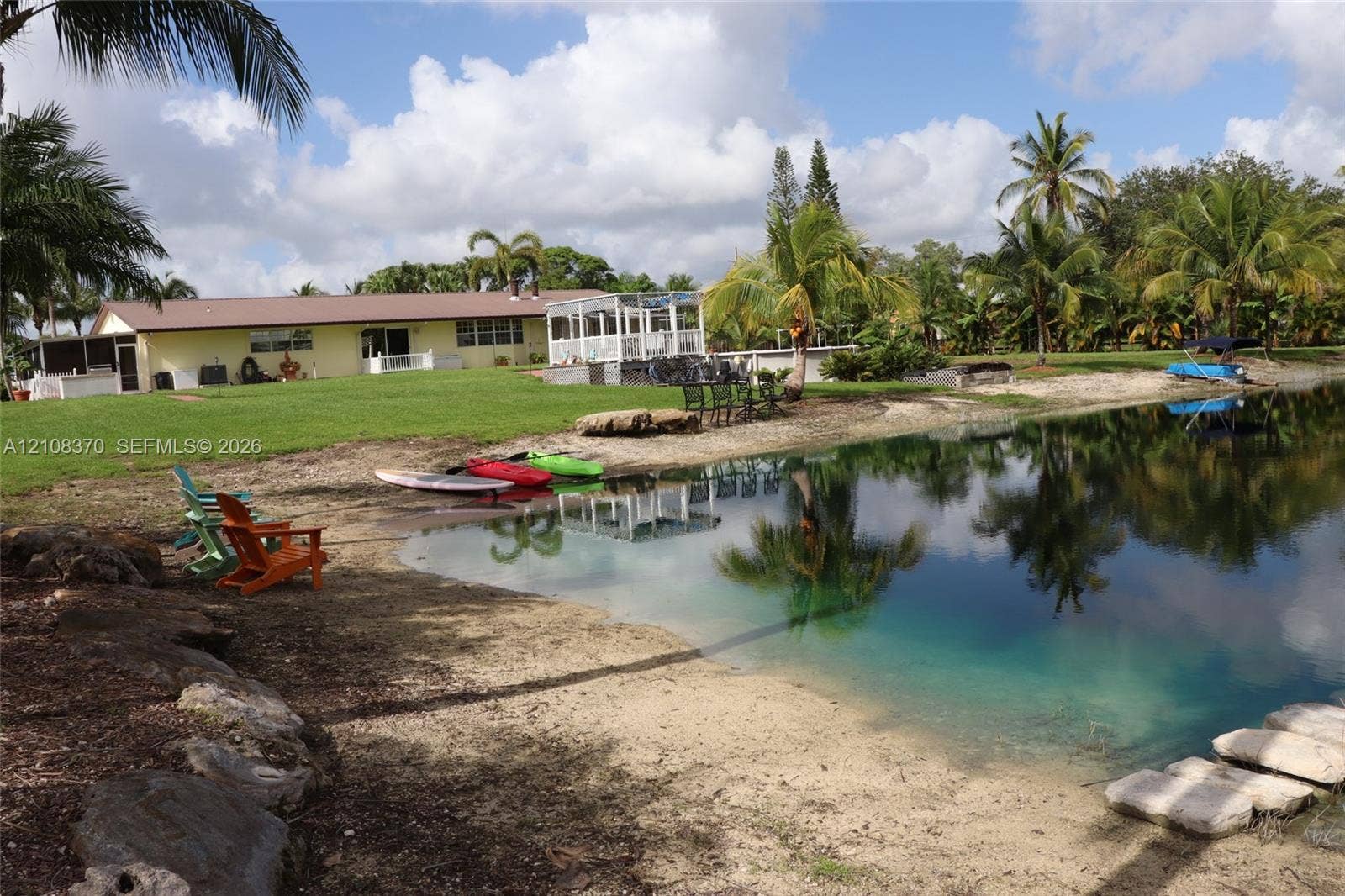 18901 SW 63rd Street, Southwest Ranches, FL 33332 Waterfront property featuring a private sandy shoreline, rock-lined banks, expansive lawn, and an elevated screened enclosure