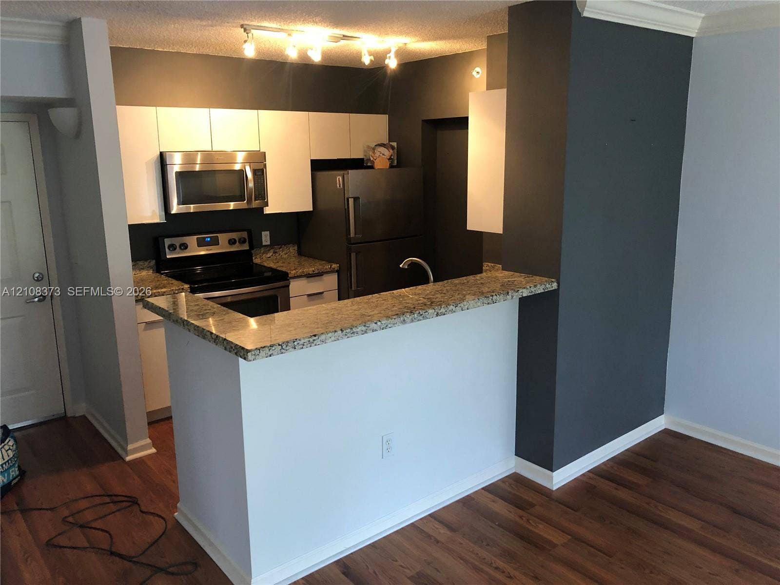 1900 Van Buren Street, #411B, Hollywood, FL 33020 Kitchen featuring white cabinetry, stone-surface breakfast bar, stainless steel appliances, and wood-finish flooring
