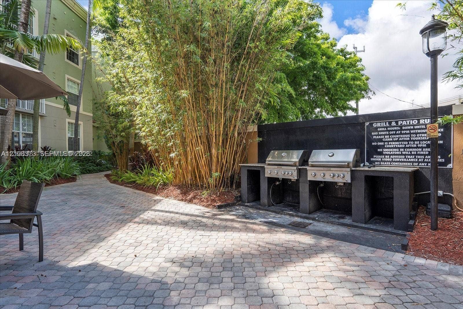 1900 Van Buren Street, #411B, Hollywood, FL 33020 Outdoor common area featuring dual built-in stainless steel gas grills, stone paver patio, and mature bamboo landscaping