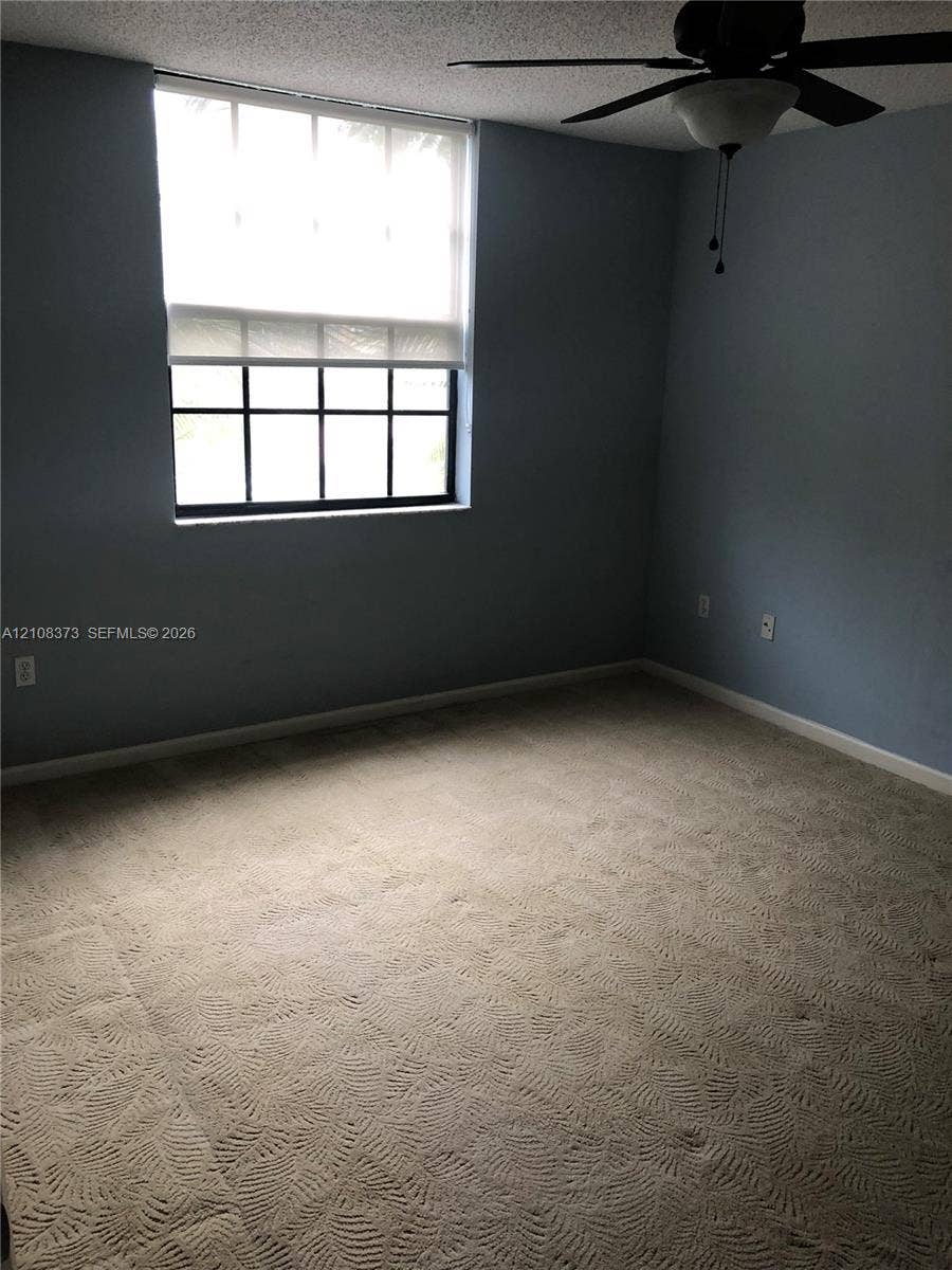 1900 Van Buren Street, #411B, Hollywood, FL 33020 Room featuring patterned carpeting, a multi-pane window with a roller shade, textured ceiling, and a ceiling fan with integrated light fixture