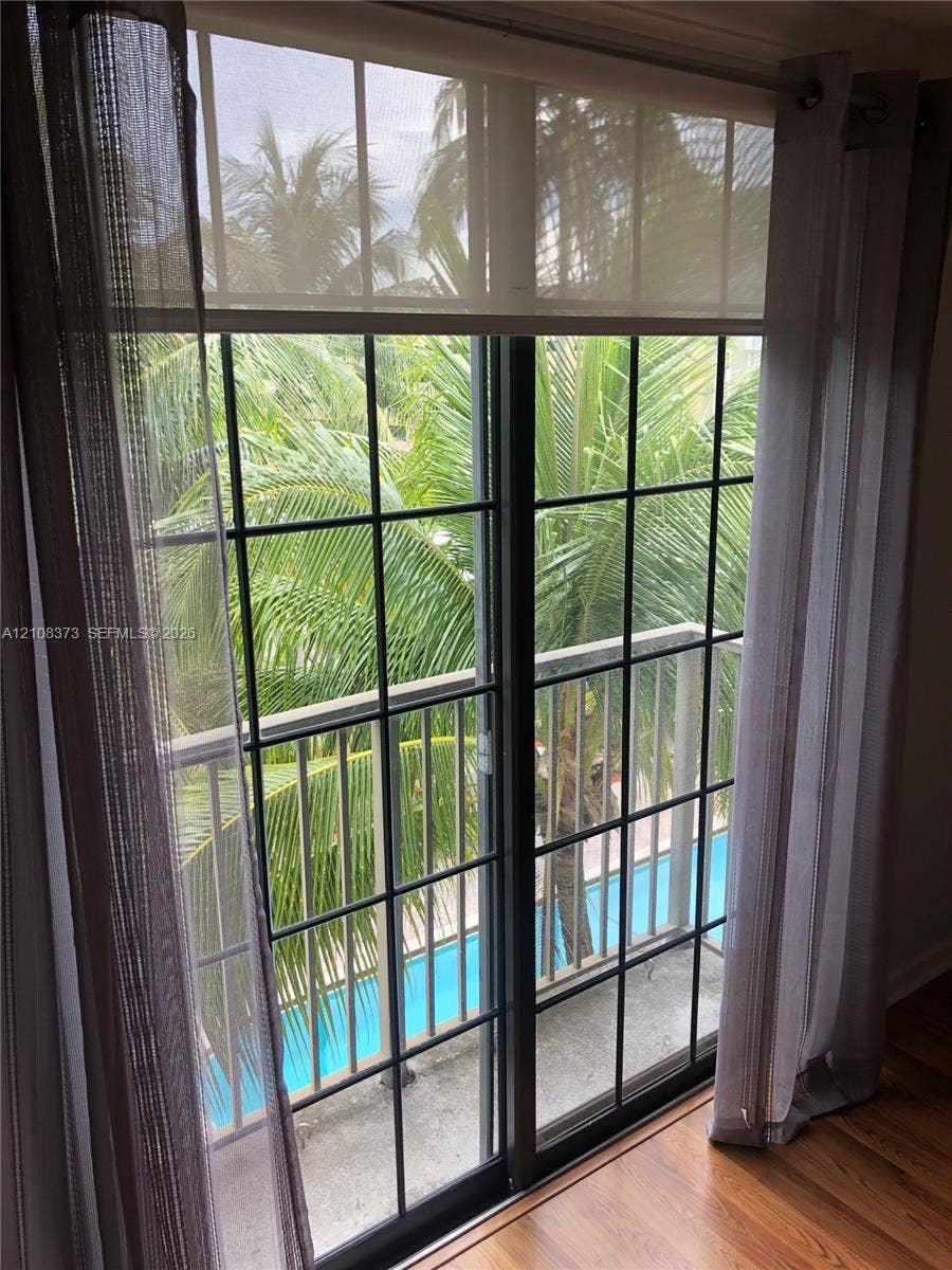 1900 Van Buren Street, #411B, Hollywood, FL 33020 Sliding glass door with a grid pattern, dark-framed balcony with metal railing, wood-finish flooring, and tropical scenery