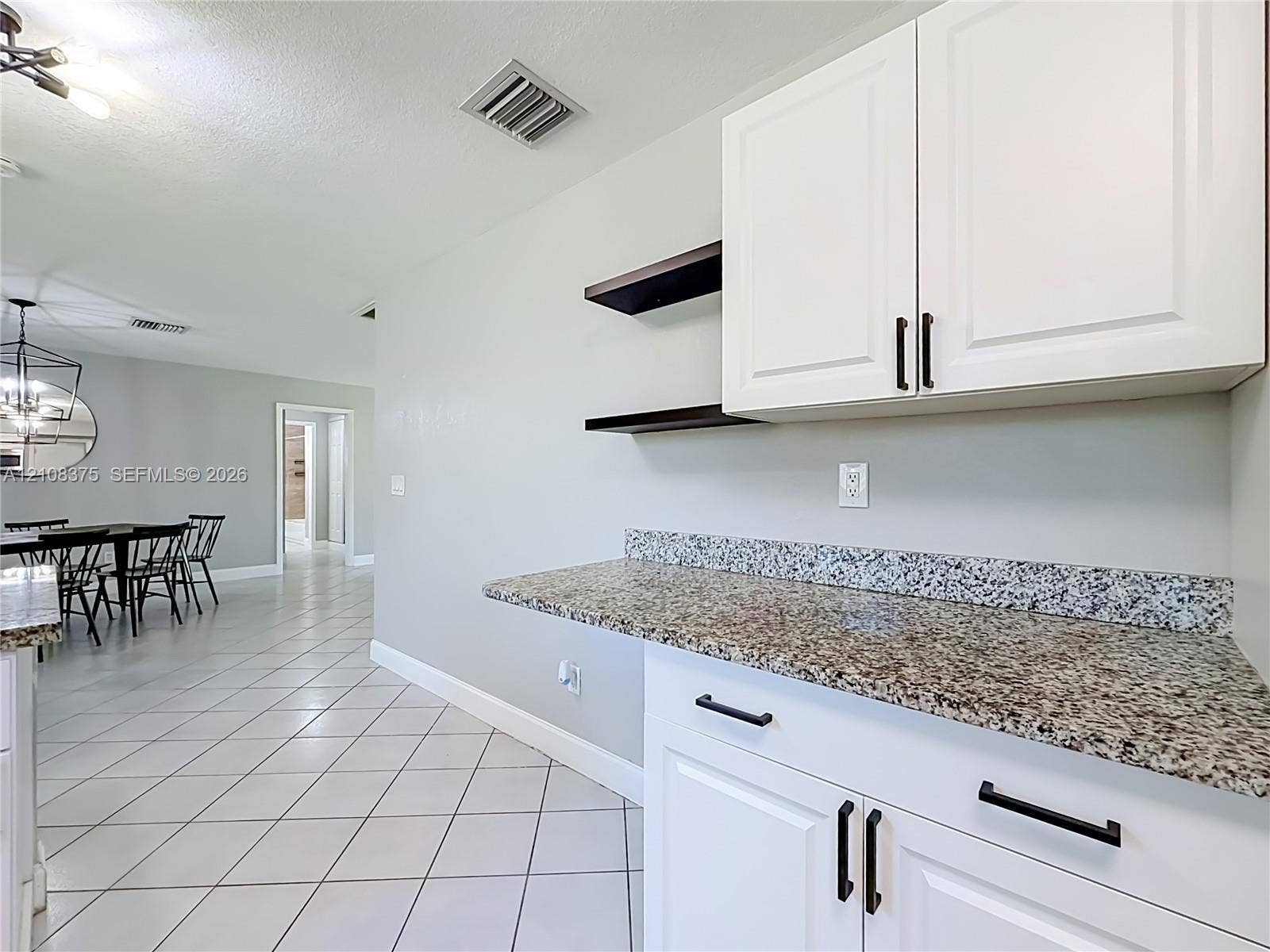3330 NE 14th Terrace, Pompano Beach, FL 33064 White cabinetry with matte black hardware, stone-finish countertops, floating shelving, and tile flooring