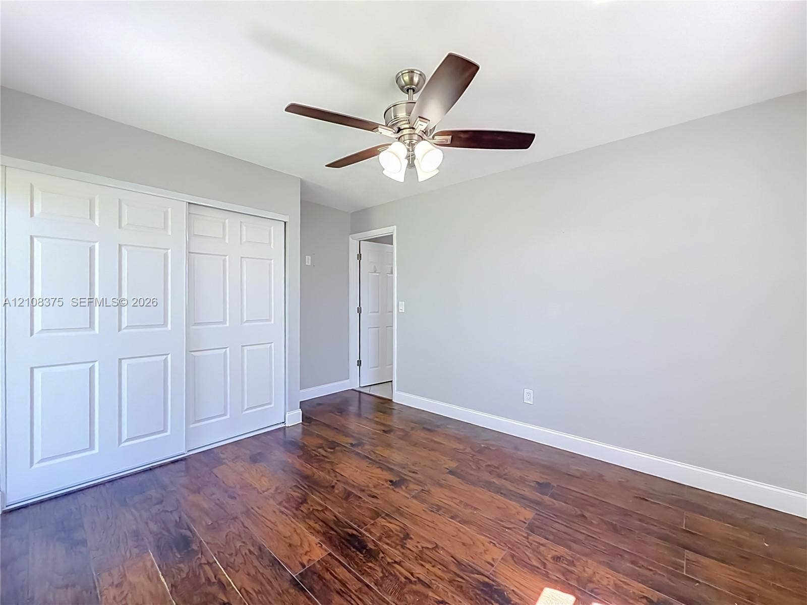 3330 NE 14th Terrace, Pompano Beach, FL 33064 Room featuring wood-finish flooring, a brushed-nickel ceiling fan with a three-light fixture, and a sliding-door closet with white six-panel doors
