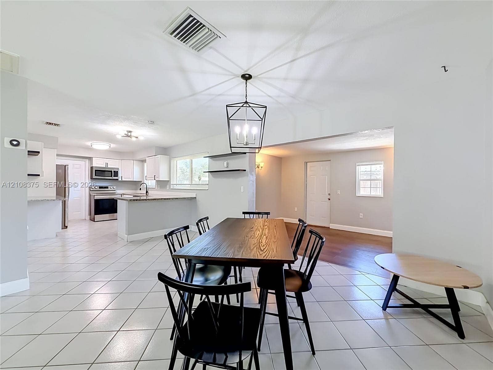 3330 NE 14th Terrace, Pompano Beach, FL 33064 Open-concept floor plan featuring ceramic tile flooring, kitchen with white cabinetry, stone-finish countertops, stainless steel appliances, and a geometric metal pendant light fixture