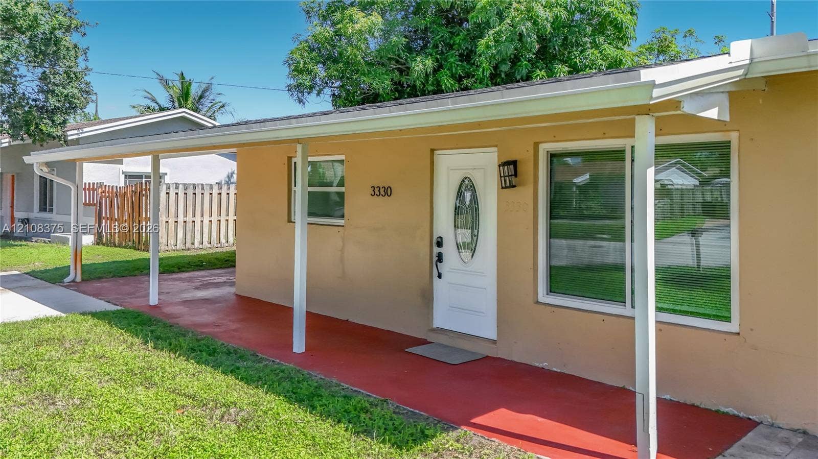 3330 NE 14th Terrace, Pompano Beach, FL 33064 Exterior facade featuring a covered porch with painted concrete flooring, white structural columns, a central entry door with a decorative oval window, and large rectangular windows
