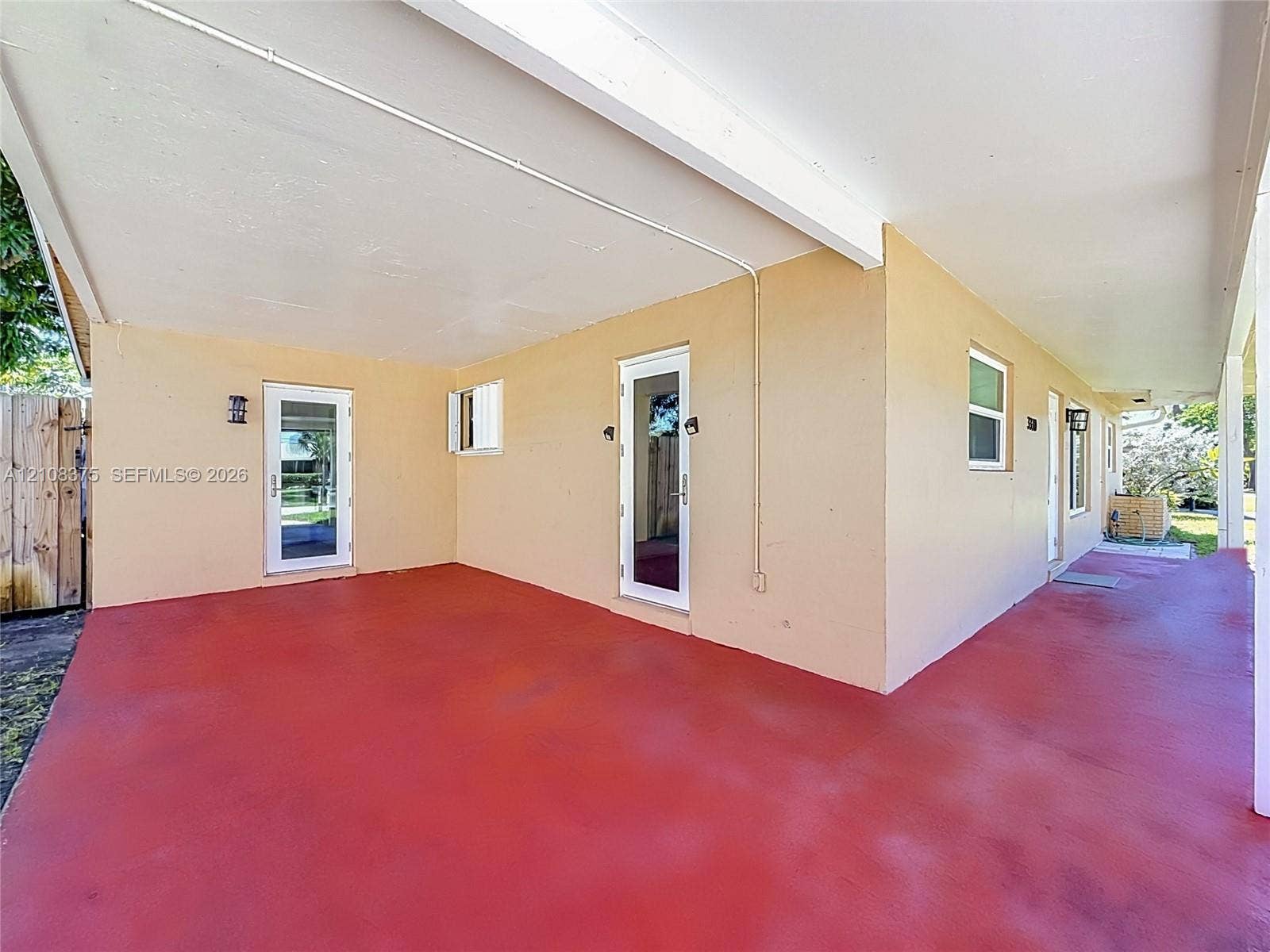3330 NE 14th Terrace, Pompano Beach, FL 33064 Covered patio with painted concrete flooring, stucco exterior walls, multiple glass-panel entry doors, and wall-mounted exterior light fixtures