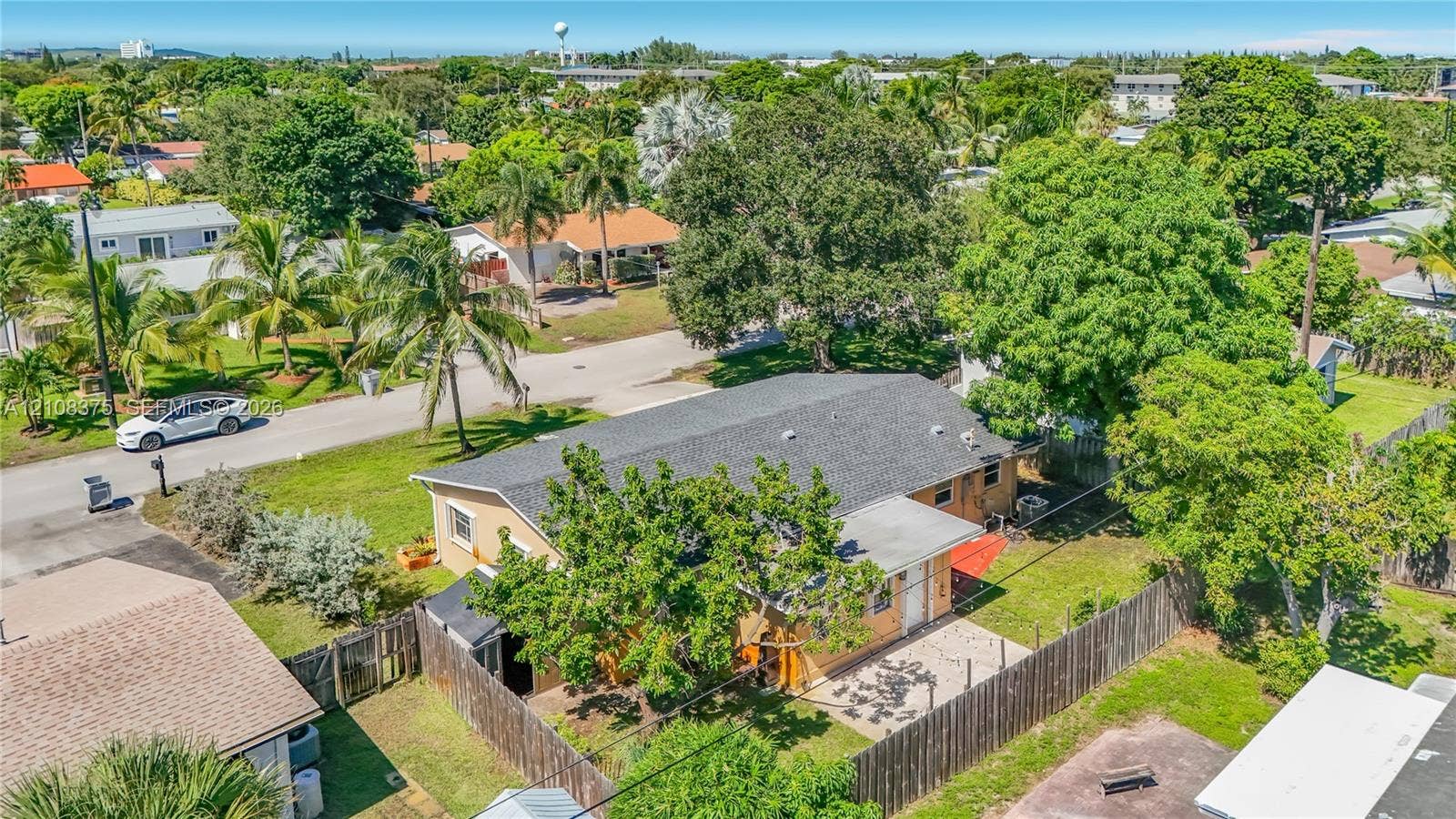 3330 NE 14th Terrace, Pompano Beach, FL 33064 Aerial perspective featuring a single-story residence with a shingled gable roof, exterior patio, wood-style privacy fencing, and mature landscaping