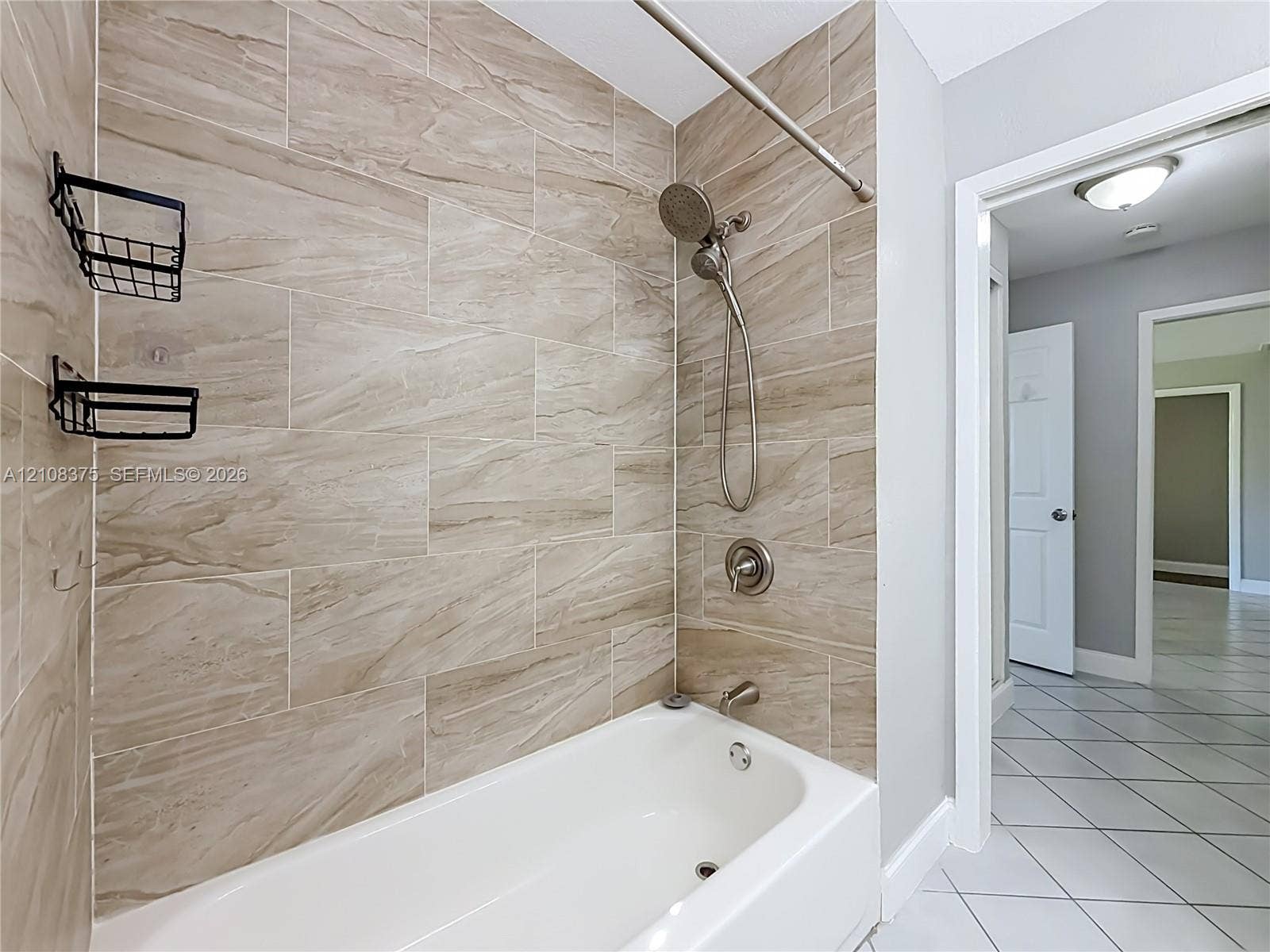 3330 NE 14th Terrace, Pompano Beach, FL 33064 Bathtub and shower combination featuring large-format ceramic tile surround, brushed nickel hardware, and a handheld shower fixture