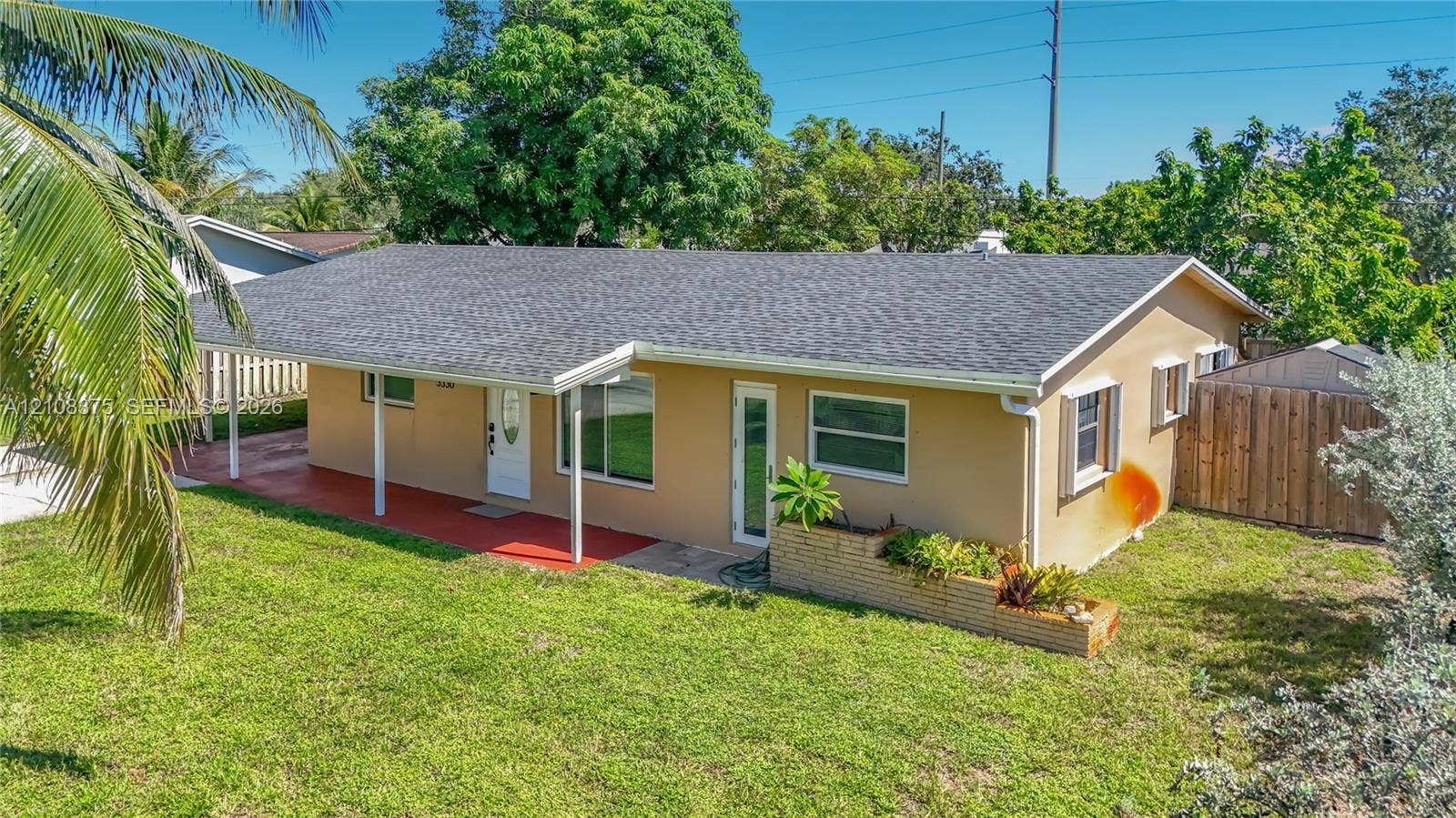 3330 NE 14th Terrace, Pompano Beach, FL 33064 Single-story exterior featuring a covered carport, shingled roof, horizontal siding, masonry planter box, and a fenced backyard
