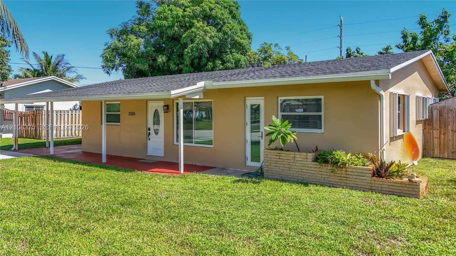 3330 NE 14th Terrace, Pompano Beach, FL 33064 Single-story exterior featuring a covered front porch, light-toned stucco facade, multi-pane windows, and a raised brick planter bed