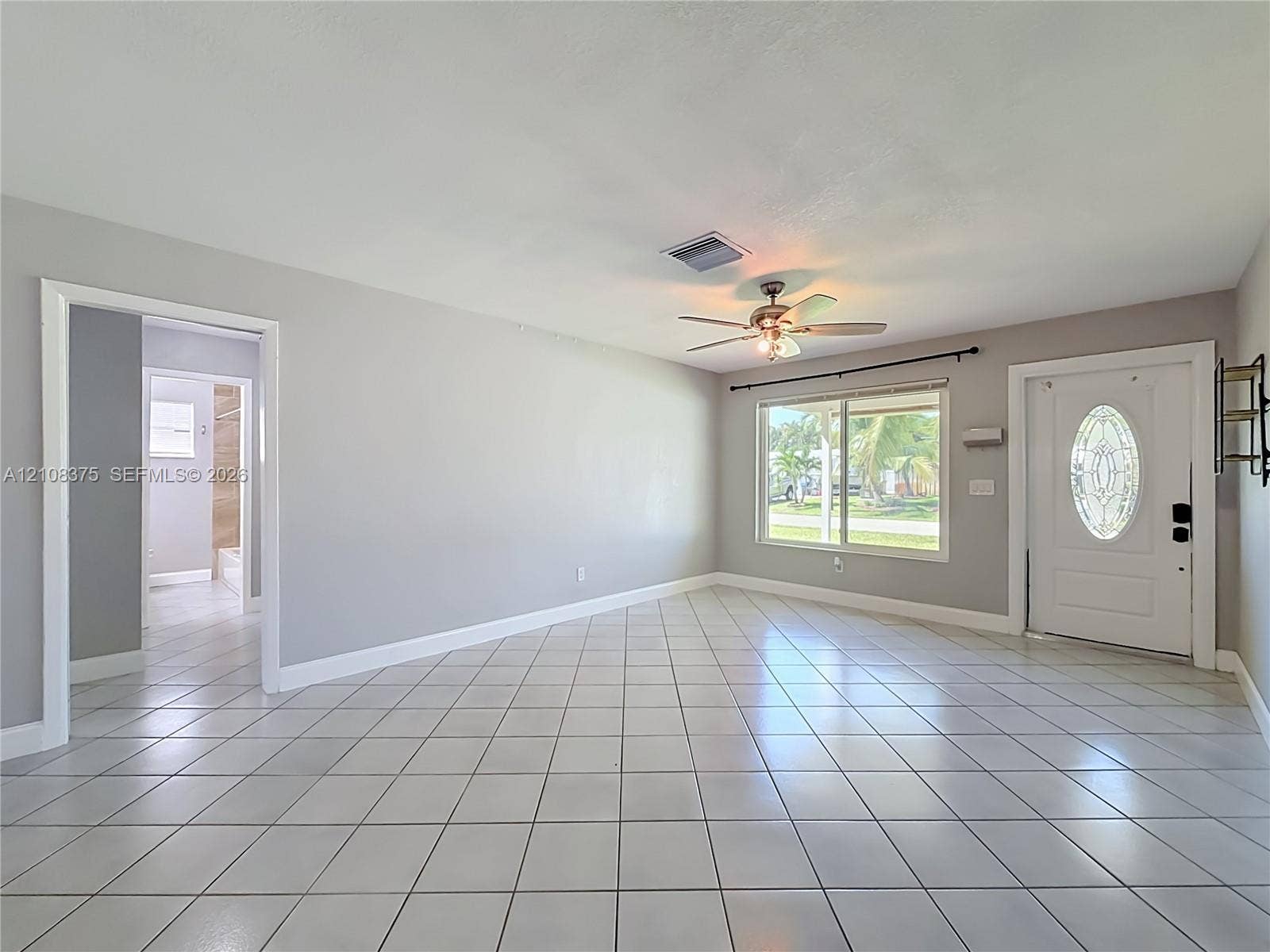 3330 NE 14th Terrace, Pompano Beach, FL 33064 Neutral-toned interior space featuring white floor tiles, a ceiling fan with integrated lighting, and an entry door with an oval glass insert