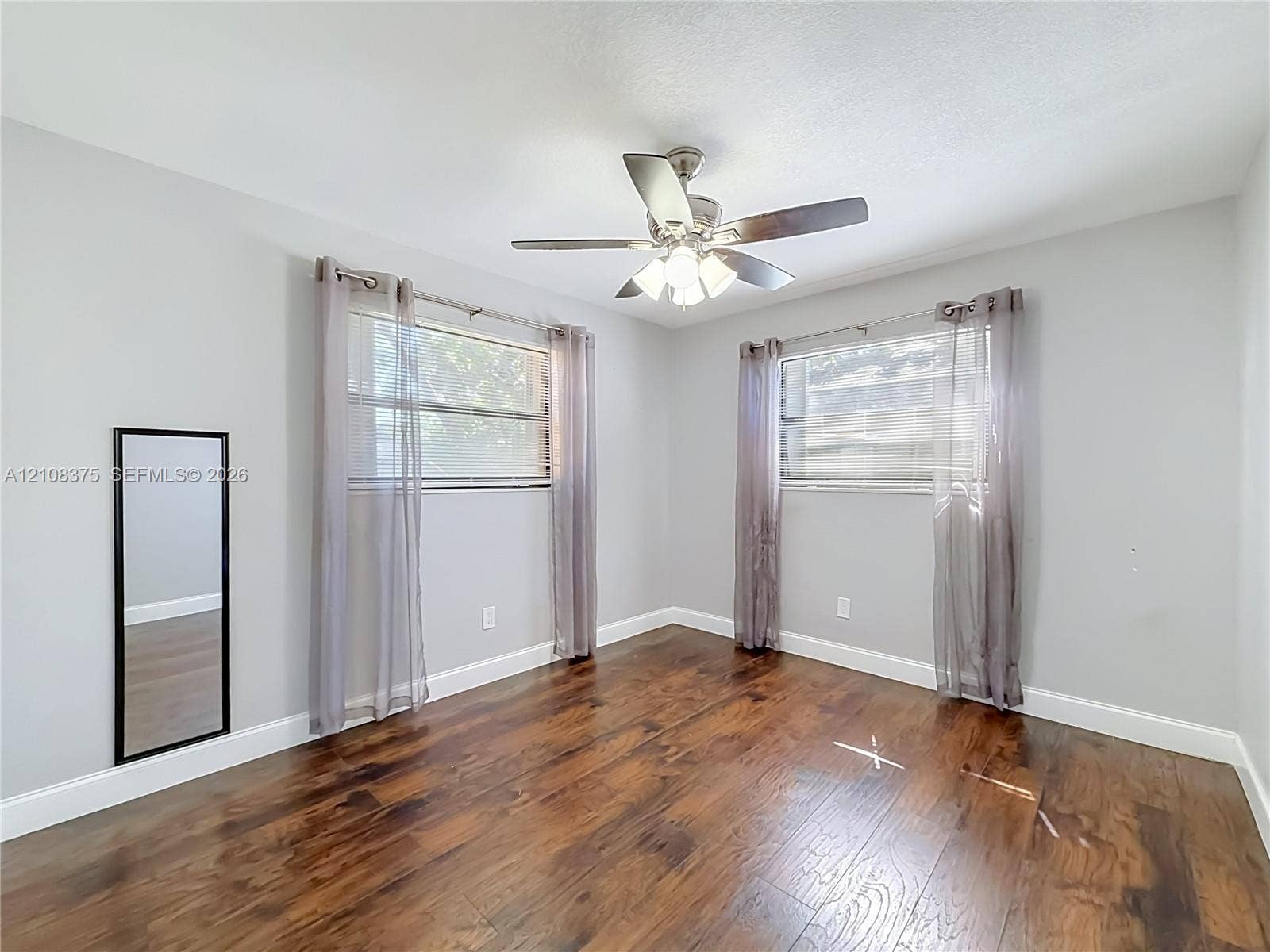 3330 NE 14th Terrace, Pompano Beach, FL 33064 Wood-finish flooring, dual windows with horizontal blinds, and a central ceiling fan with integrated lighting