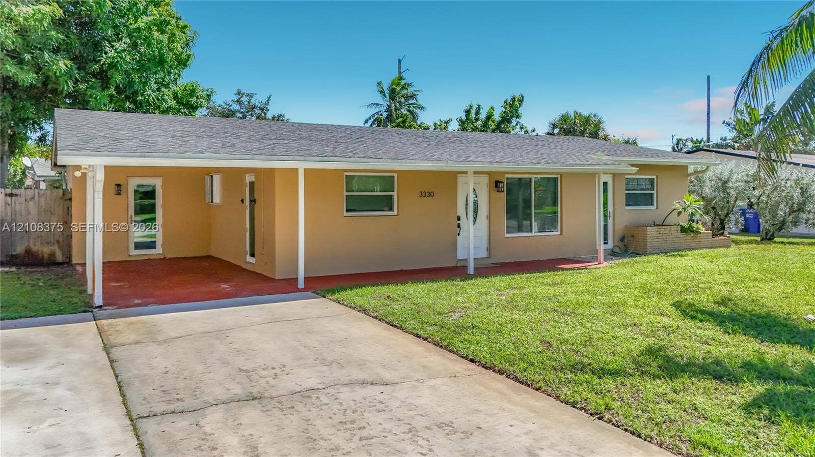 3330 NE 14th Terrace, Pompano Beach, FL 33064 Single-story residence featuring a covered carport, concrete driveway, asphalt shingle roof, and expansive front lawn