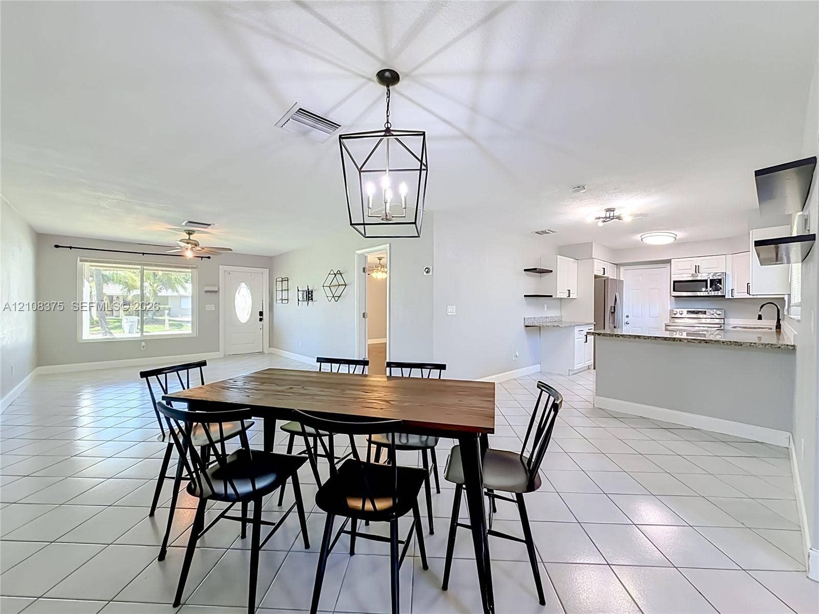 3330 NE 14th Terrace, Pompano Beach, FL 33064 Open-concept interior featuring light-toned tile flooring, kitchen with peninsula counter, built-in cabinetry, and geometric lantern-style pendant lighting