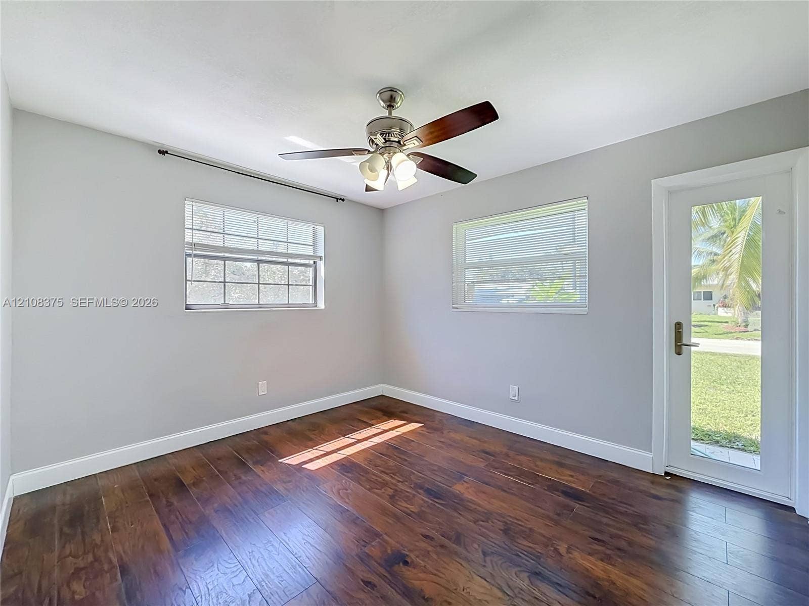 3330 NE 14th Terrace, Pompano Beach, FL 33064 Room featuring wood-finish flooring, a multi-blade ceiling fan with integrated lighting, dual windows with horizontal blinds, and a glass-paneled exterior door