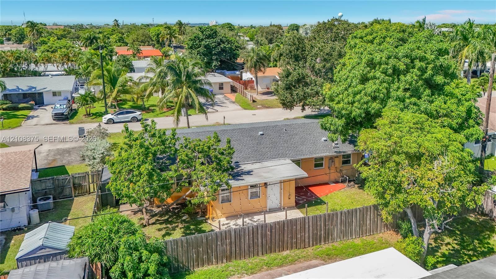 3330 NE 14th Terrace, Pompano Beach, FL 33064 Single-story exterior featuring a shingle roof, concrete patio, perimeter wood fencing, and mature landscaping