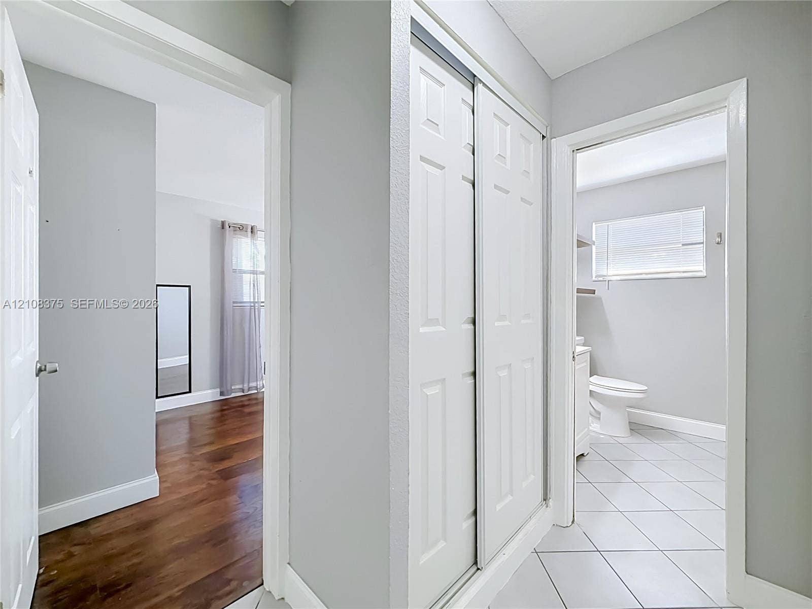 3330 NE 14th Terrace, Pompano Beach, FL 33064 Hallway featuring white dual-panel sliding closet doors, wood-finish flooring, and porcelain tile flooring in the entryways