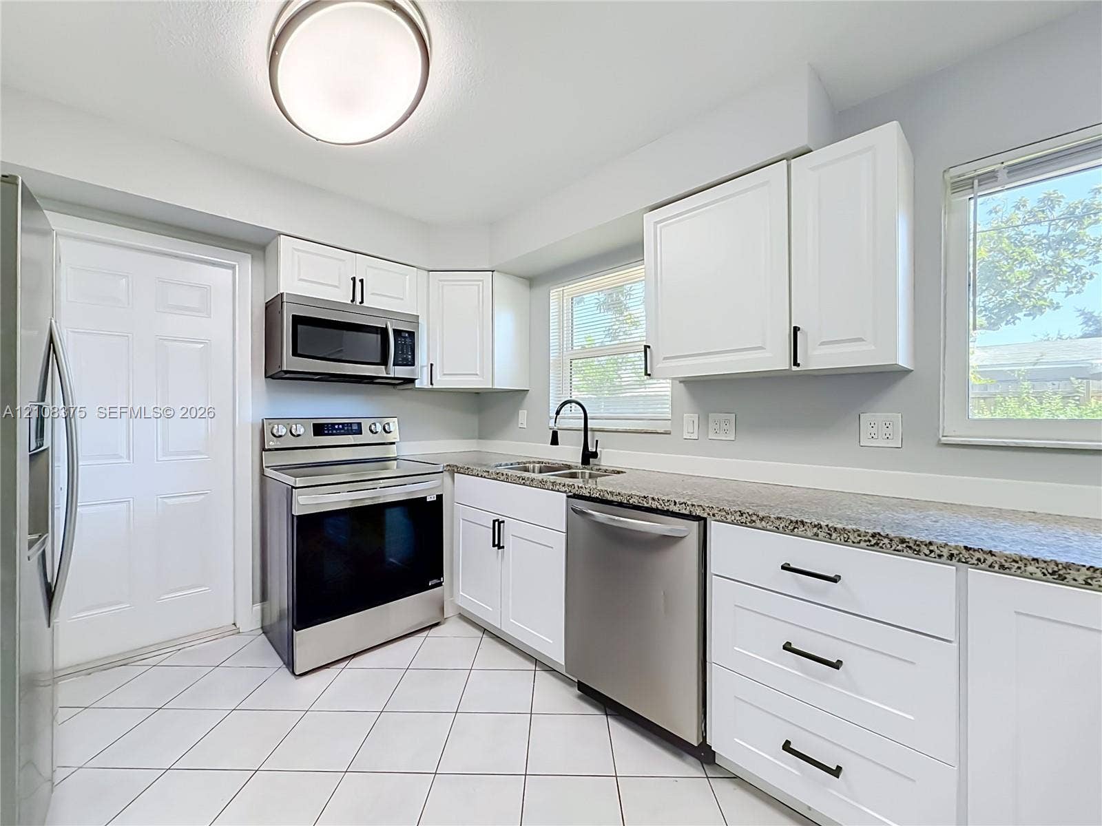 3330 NE 14th Terrace, Pompano Beach, FL 33064 Kitchen featuring white shaker-style cabinetry, stone-finish countertops, stainless steel appliances, matte black hardware, and diagonal-set tile flooring