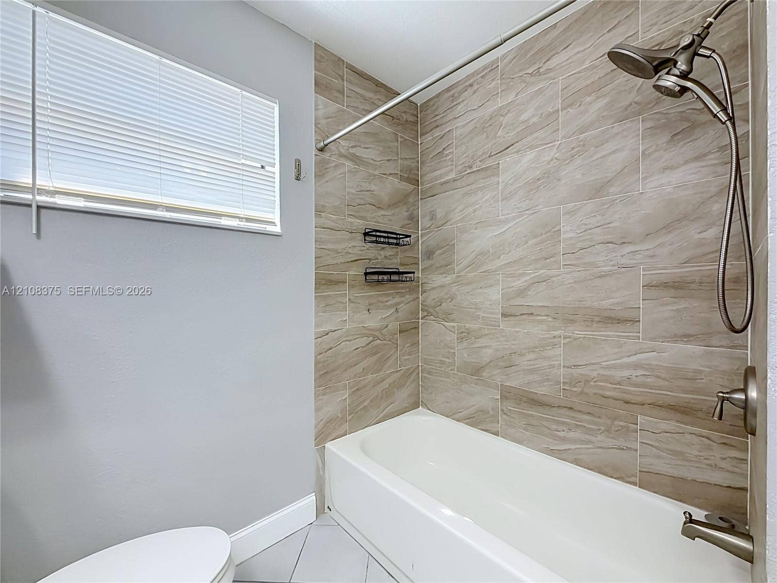 3330 NE 14th Terrace, Pompano Beach, FL 33064 Bathtub featuring large-format ceramic tile surround with natural patterning, brushed-nickel shower hardware, and a horizontal window