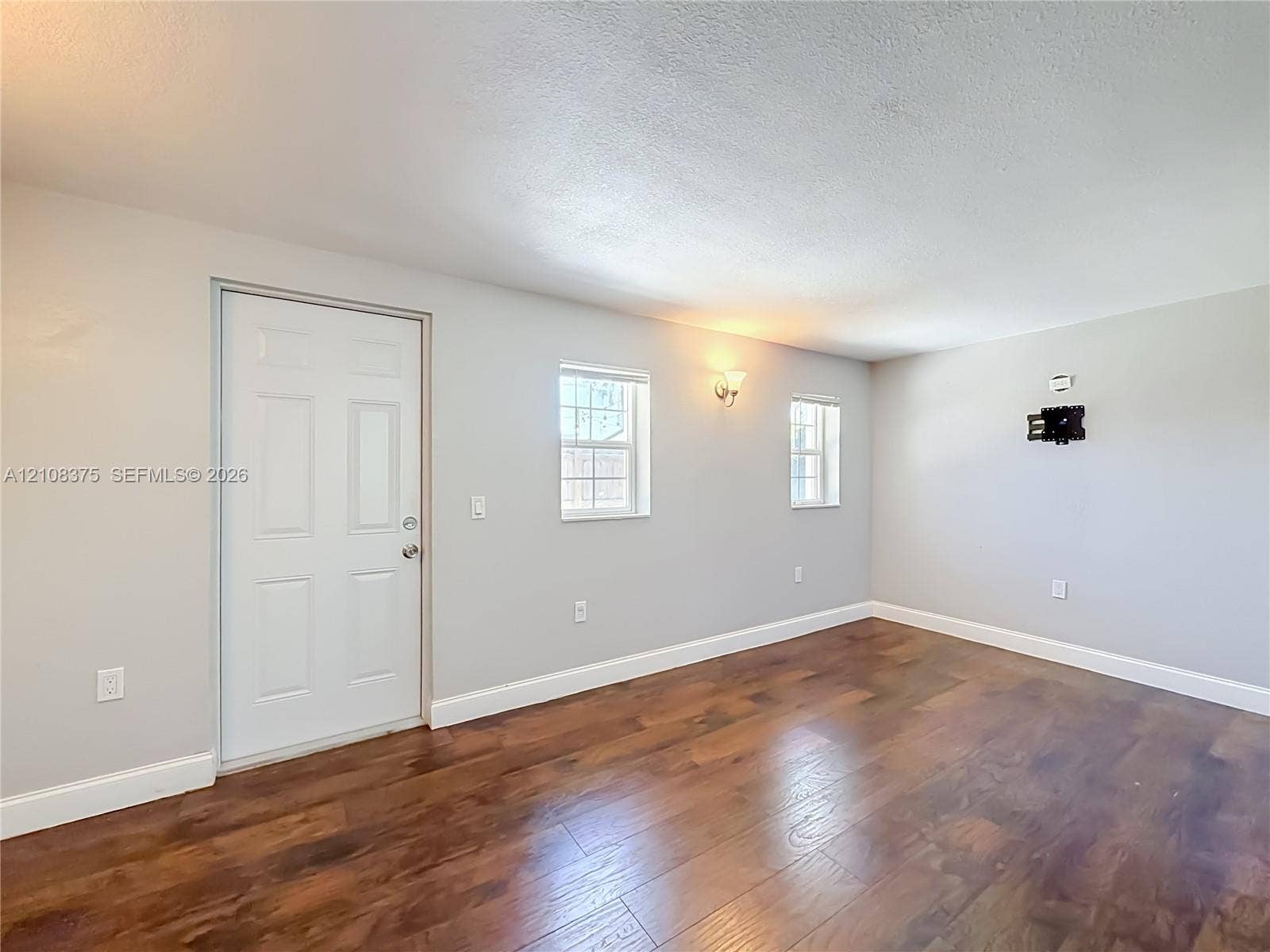 3330 NE 14th Terrace, Pompano Beach, FL 33064 Interior space featuring wood-finish flooring, neutral wall paint, two double-hung windows, a solid-core entry door, and wall-mounted lighting