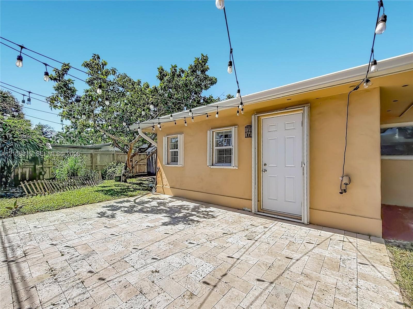 3330 NE 14th Terrace, Pompano Beach, FL 33064 Rear patio featuring stone paver flooring, exterior wall-mounted string lighting, and wood fencing