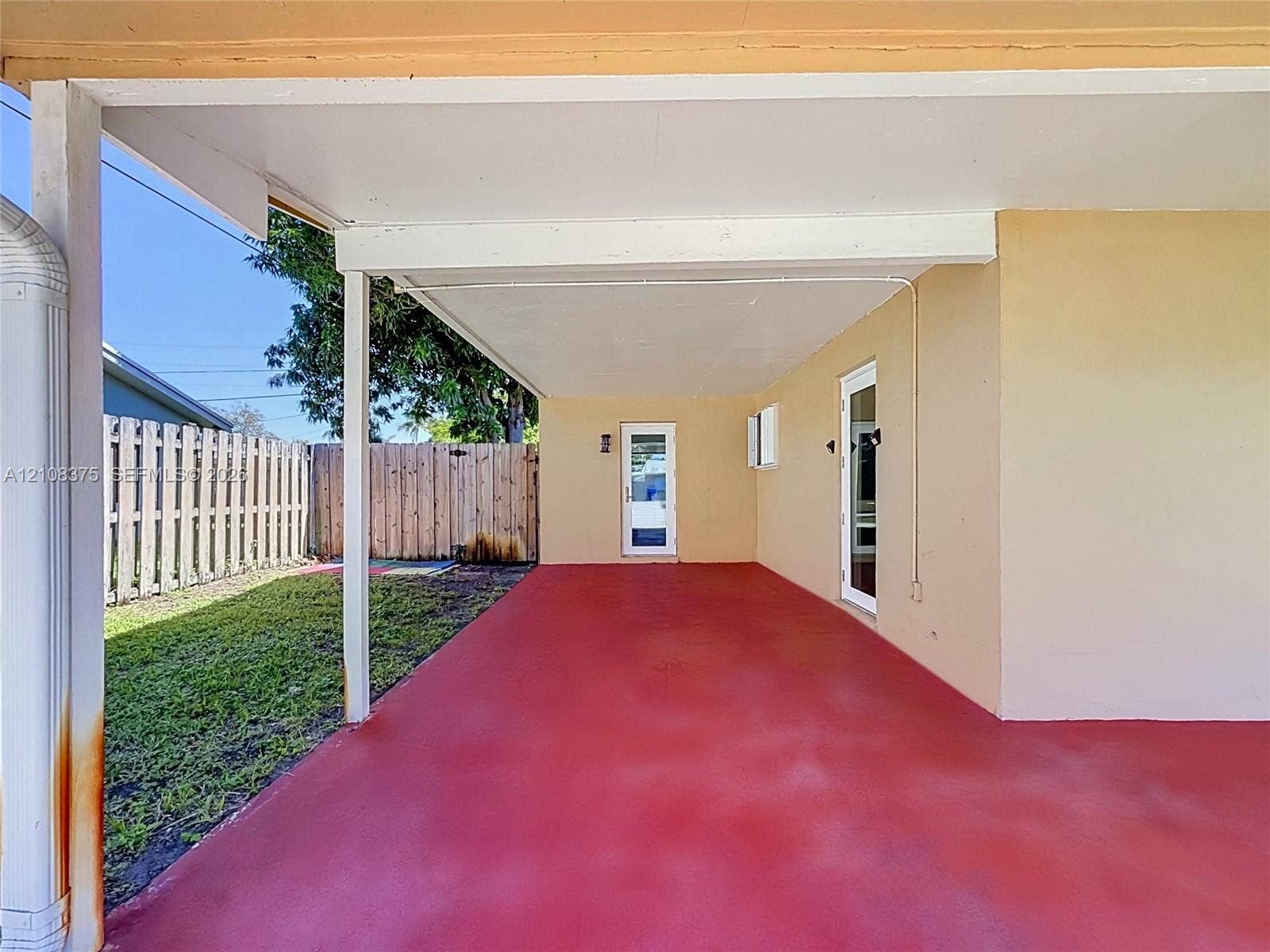 3330 NE 14th Terrace, Pompano Beach, FL 33064 Covered exterior patio with painted concrete flooring, two glass-panel entry doors, and a wood-slat privacy fence
