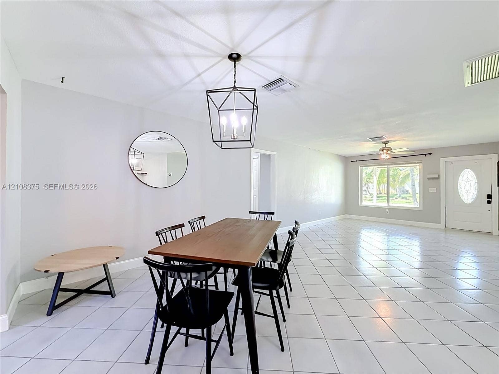 3330 NE 14th Terrace, Pompano Beach, FL 33064 Large-format tile flooring, geometric metal cage pendant lighting, round wall mirror, and panel door with decorative glass insert