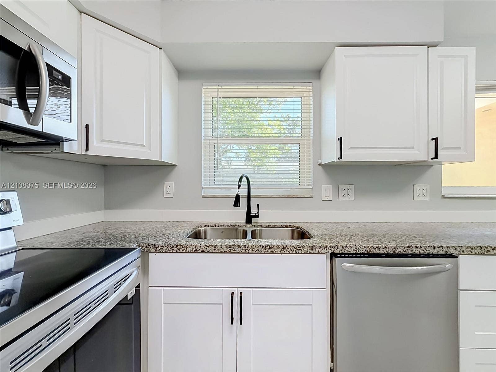 3330 NE 14th Terrace, Pompano Beach, FL 33064 Kitchen featuring white shaker-style cabinetry, stone-finish countertops, stainless steel appliances, dual-basin stainless steel sink with matte black gooseneck faucet, and a window with blinds