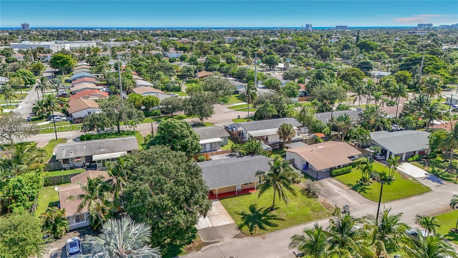 3330 NE 14th Terrace, Pompano Beach, FL 33064 Aerial perspective of a single-story residence featuring a shingled gable roof, concrete driveway, and expansive lawn with mature palm trees