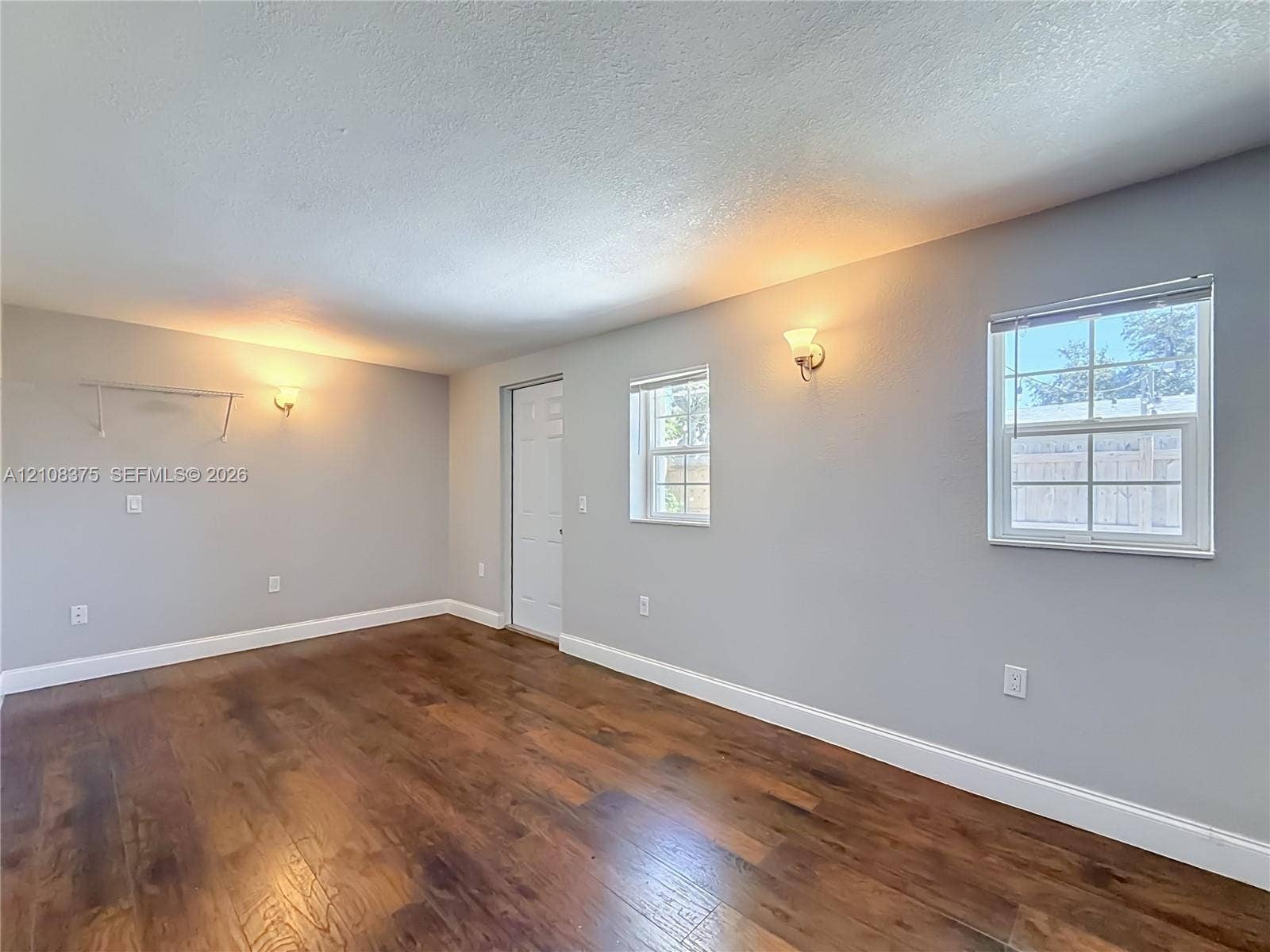 3330 NE 14th Terrace, Pompano Beach, FL 33064 Interior space featuring wood-finish flooring, neutral wall tones, dual wall-mounted light fixtures, multi-pane windows, and a panel door