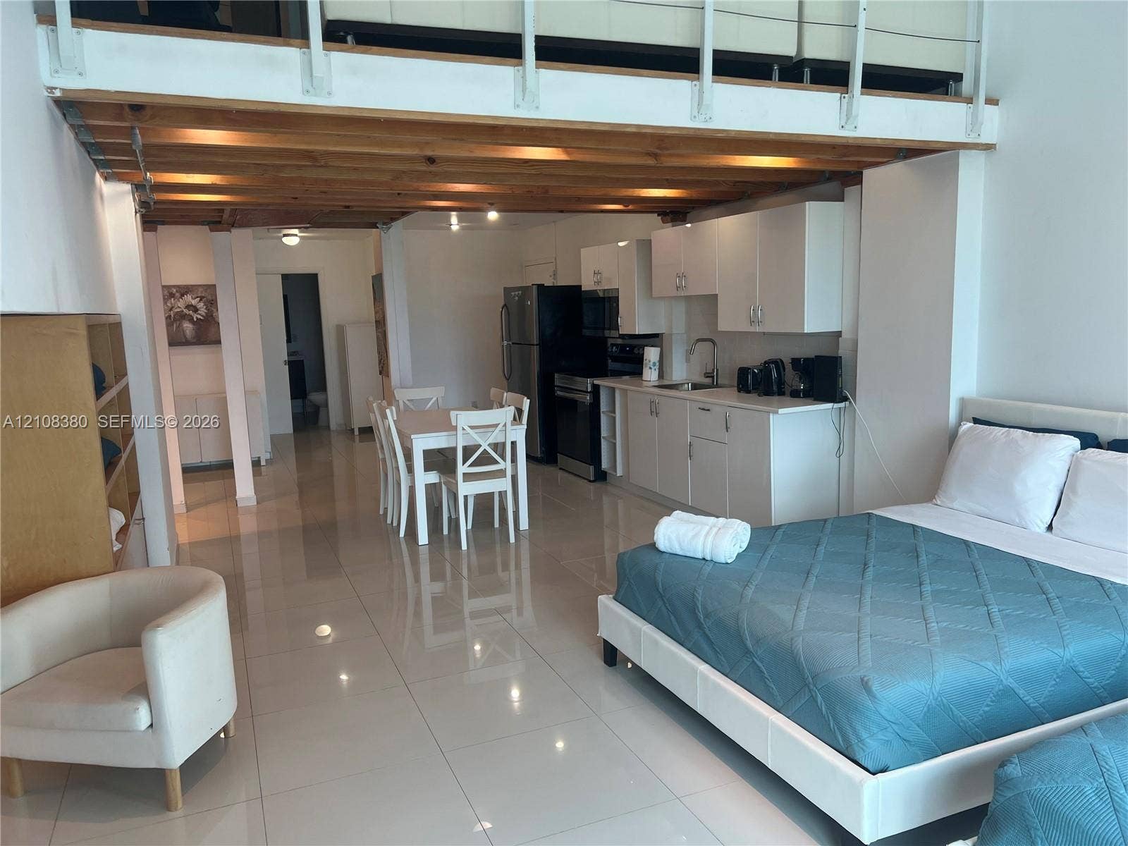 5445 Collins Avenue, #BAY11, Miami Beach, FL 33140 High-ceiling interior featuring an exposed wood-beam loft structure, polished tile flooring, white cabinetry, and recessed lighting