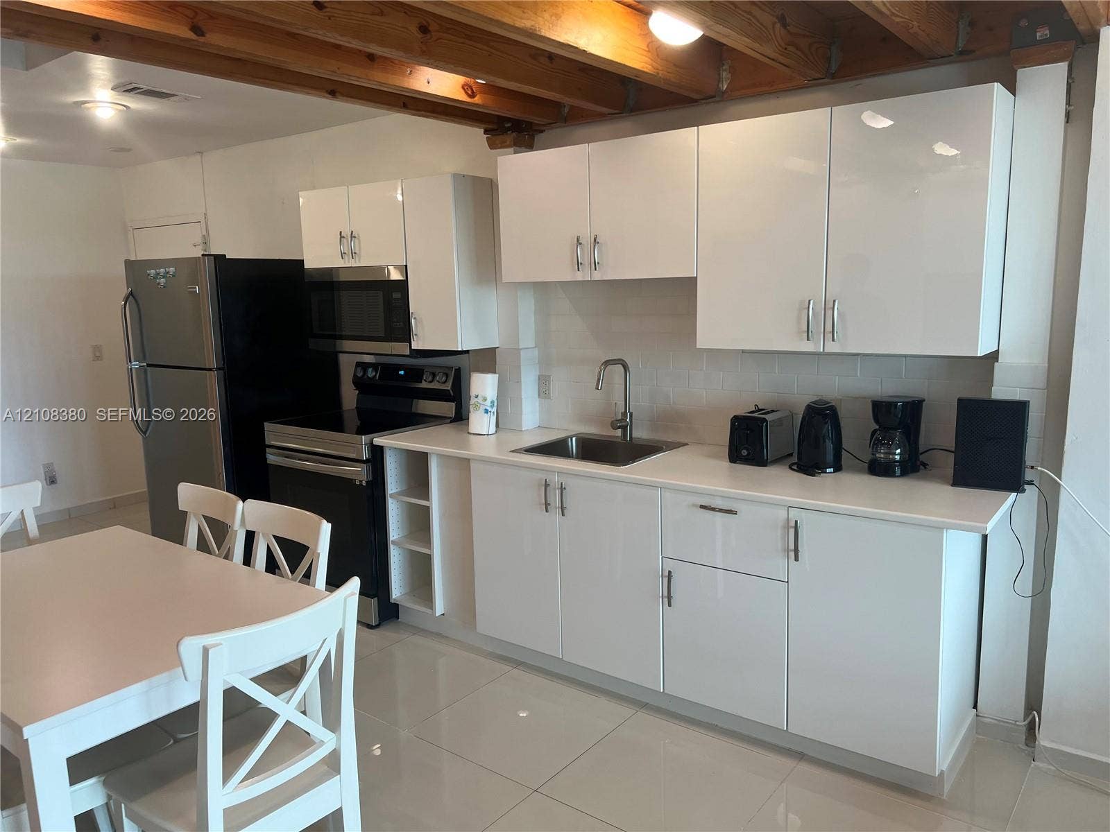 5445 Collins Avenue, #BAY11, Miami Beach, FL 33140 Kitchen featuring high-gloss white cabinetry, white stone-finish countertops, exposed wooden ceiling beams, and polished tile flooring