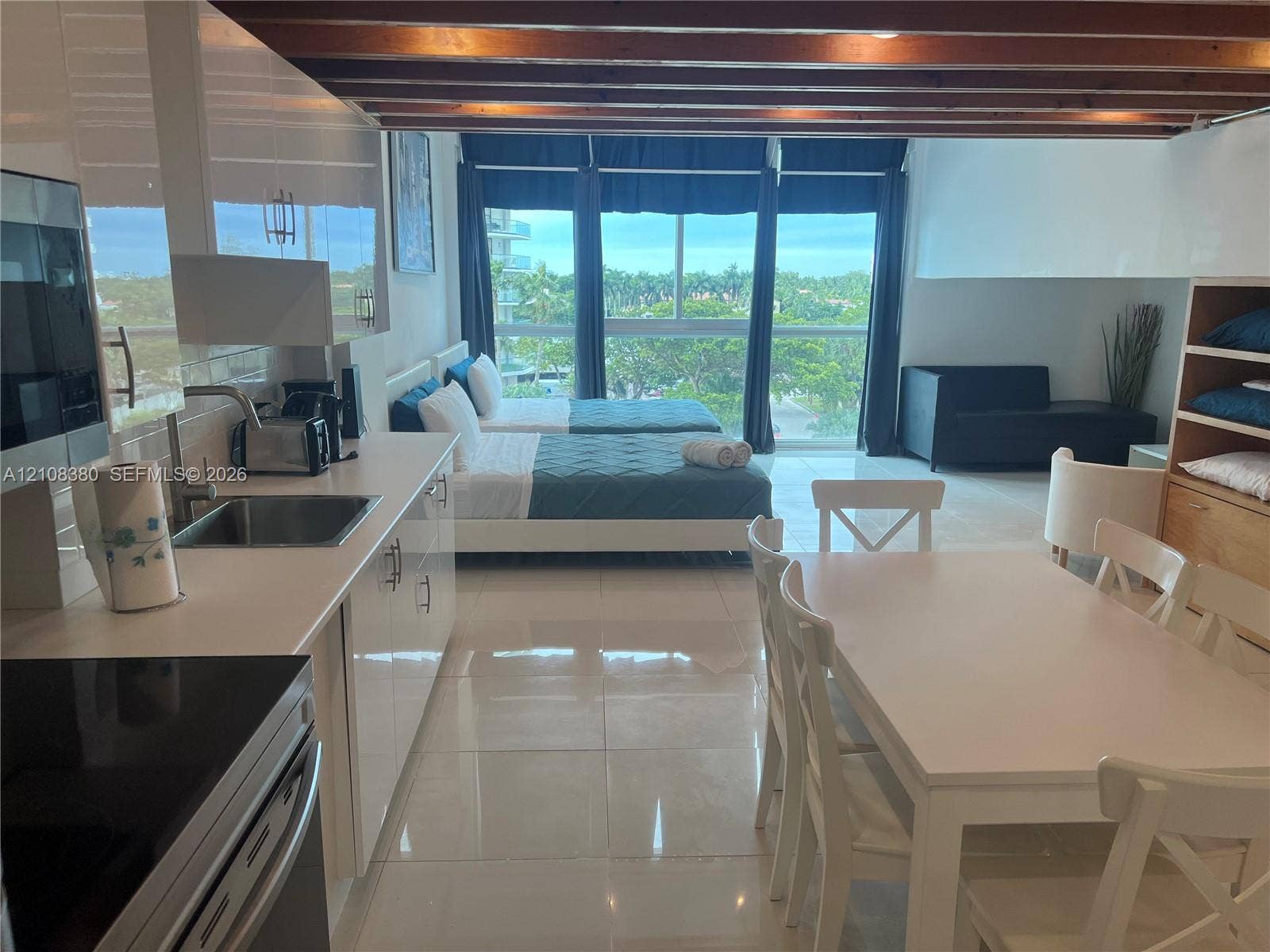 5445 Collins Avenue, #BAY11, Miami Beach, FL 33140 High-gloss cabinetry, stainless steel sink, tile flooring, exposed wood ceiling beams, and floor-to-ceiling windows