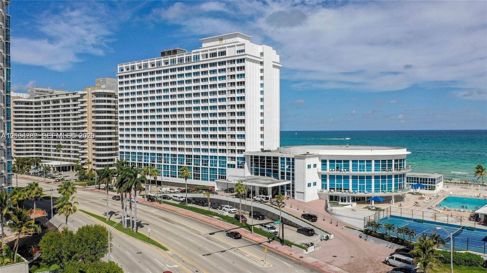 5445 Collins Avenue, #BAY11, Miami Beach, FL 33140 High-rise residential exterior featuring expansive glass facade, swimming pool, and tennis court, situated along the coastline