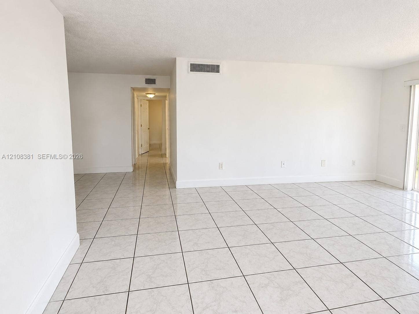 621 NW 177th Street, #101, Miami Gardens, Miami Gardens, FL 33169 Neutral-toned interior space featuring glossy, square-format ceramic tile flooring, expansive smooth-finish white walls, and a large, multi-pane window with integrated blinds
