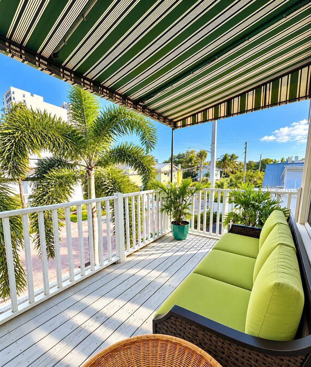 1701 S Olive Avenue, West Palm Beach, FL 33401 Covered balcony featuring white railing, light-toned wood-finish flooring, and a retractable striped awning