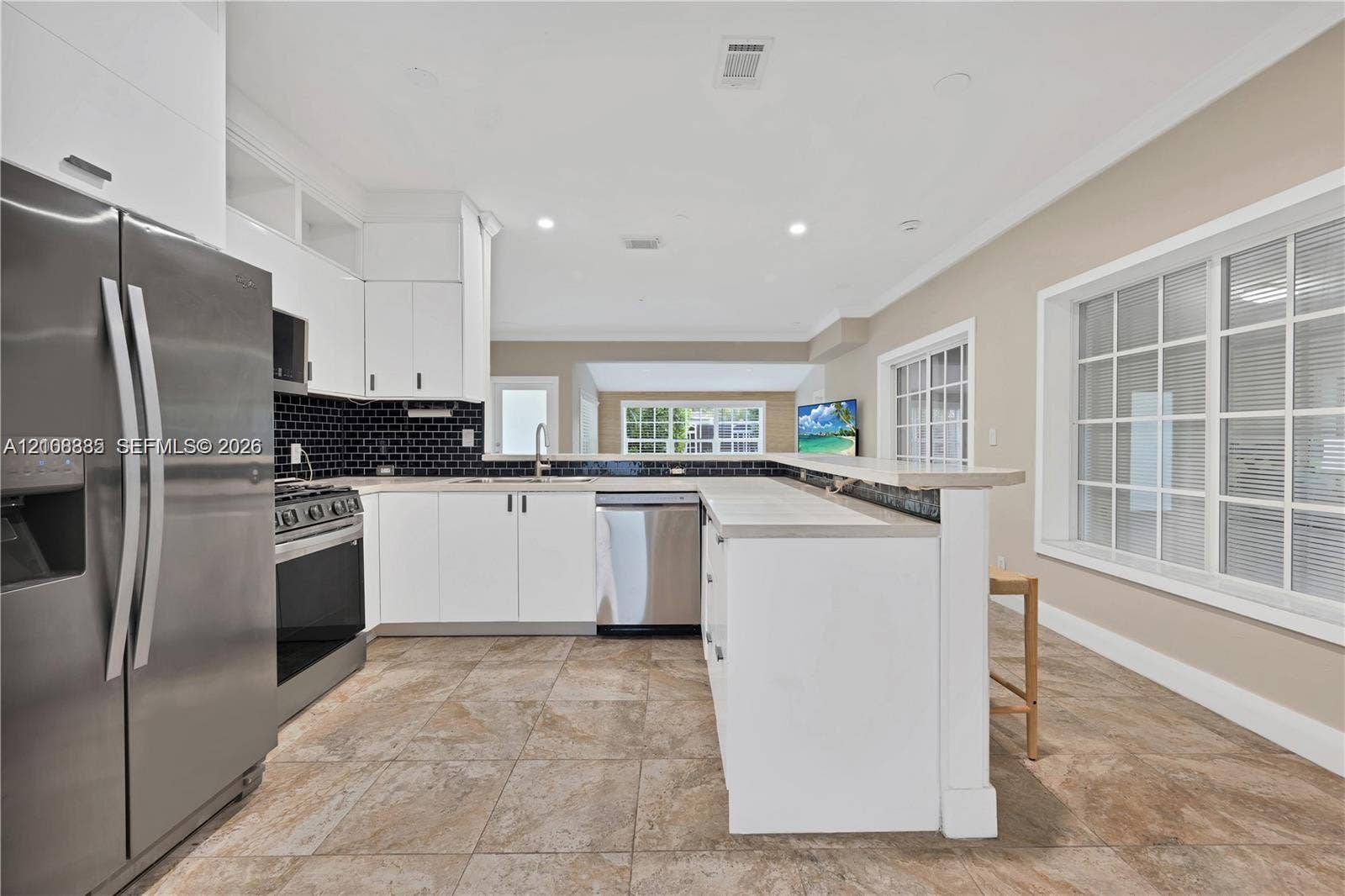 818 NE 3rd Street, Hallandale Beach, Hallandale Beach, FL 33009 Kitchen featuring white shaker cabinetry, stainless steel appliances, a black tiled backsplash, a stone-finish countertop peninsula, and ceramic tile flooring