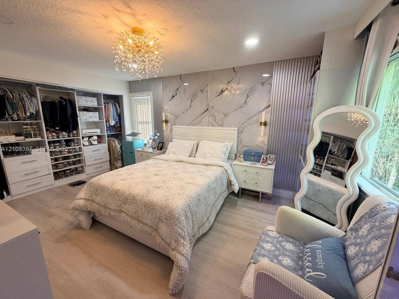 5703 NW 48th Avenue, Coconut Creek, FL 33073 Bedroom featuring wood-finish flooring, a stone-patterned accent wall, a multi-tiered crystal chandelier, recessed lighting, and built-in closet cabinetry