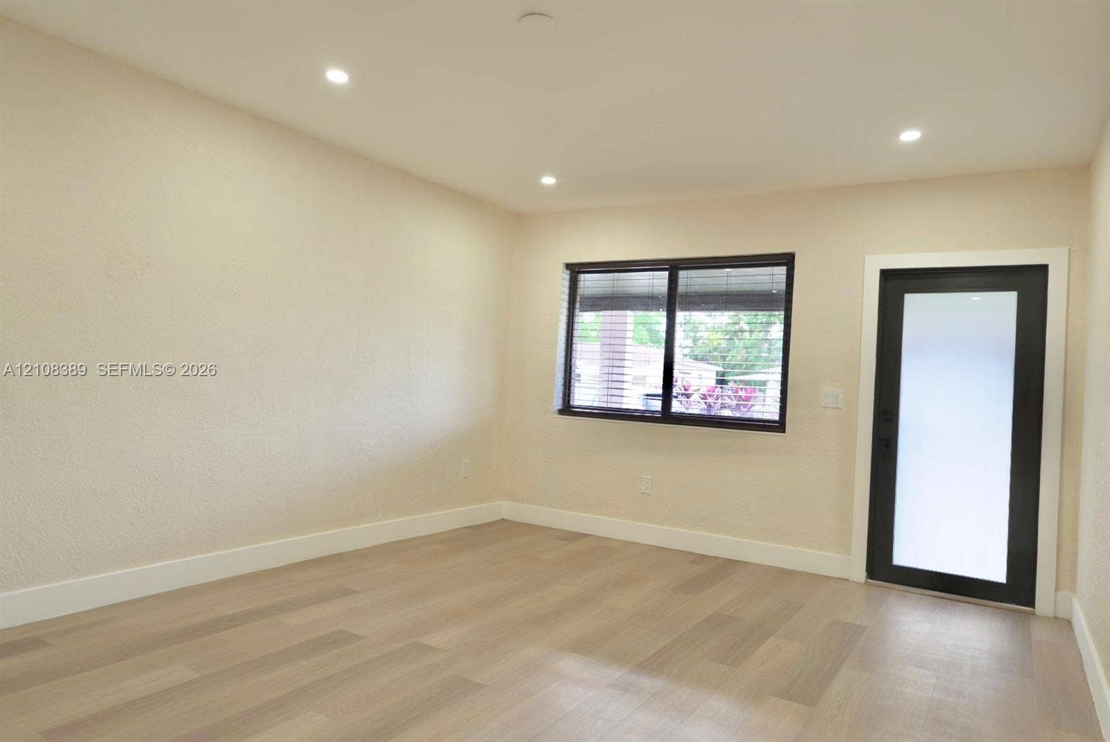 Interior space featuring wood-finish flooring, recessed lighting, textured walls, a single-pane window with dark trim, and a glass-paneled exterior door