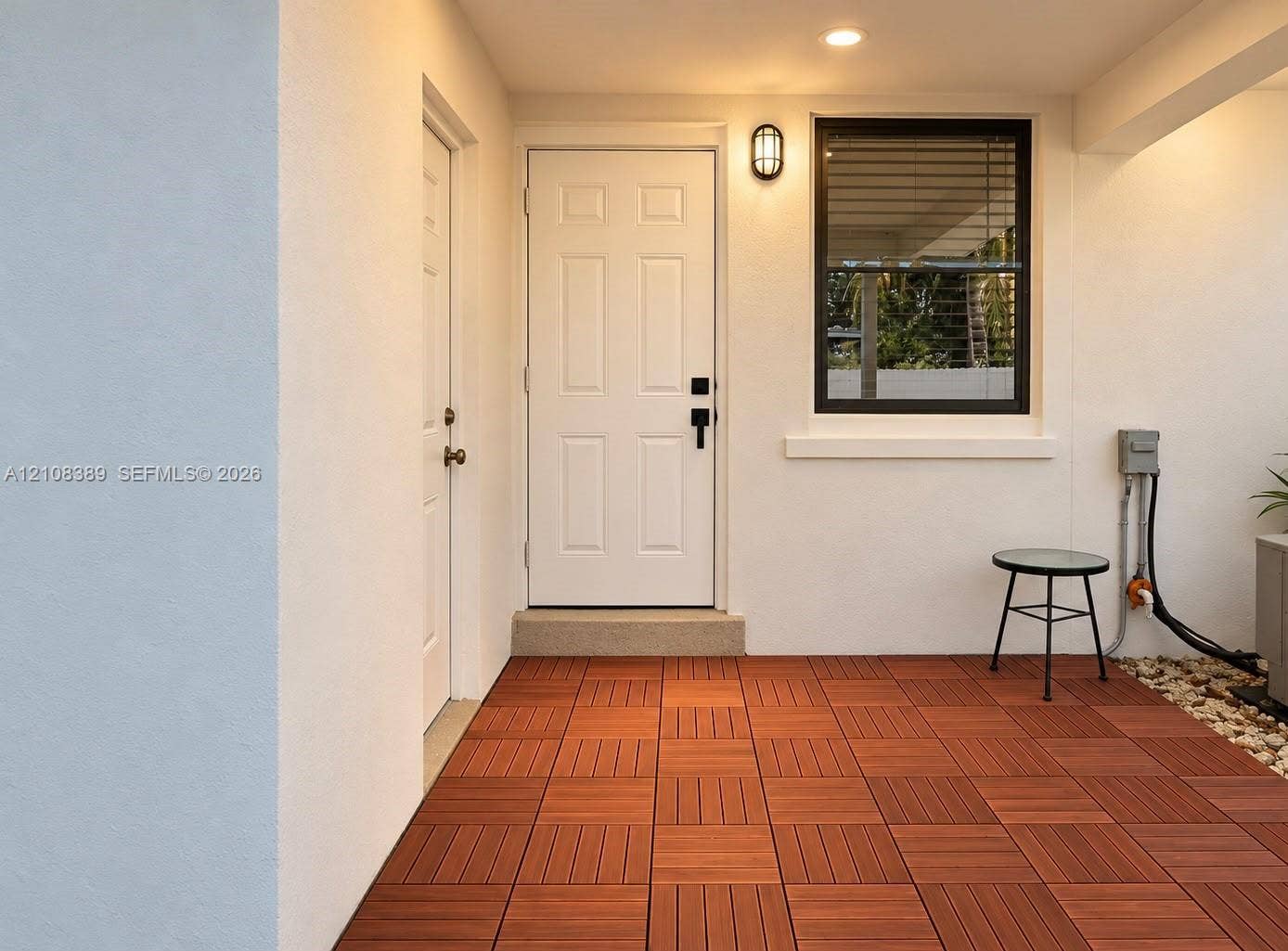 Covered patio featuring wood-finish decking, recessed ceiling lighting, a white six-panel entry door, and a black-framed window